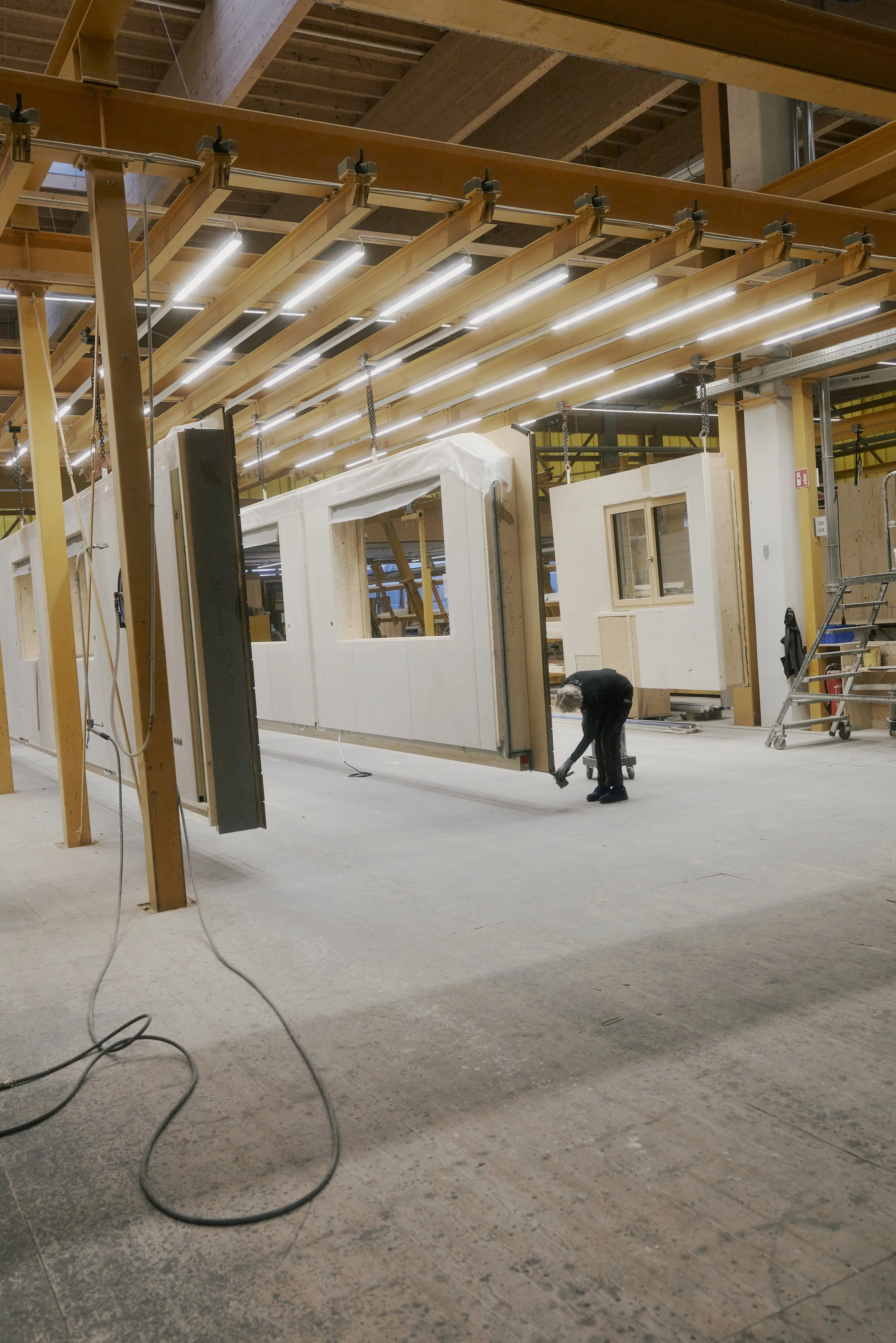 Fabrikhalle mit Holzrahmenkonstruktionen und einer Person, die daran arbeitet.