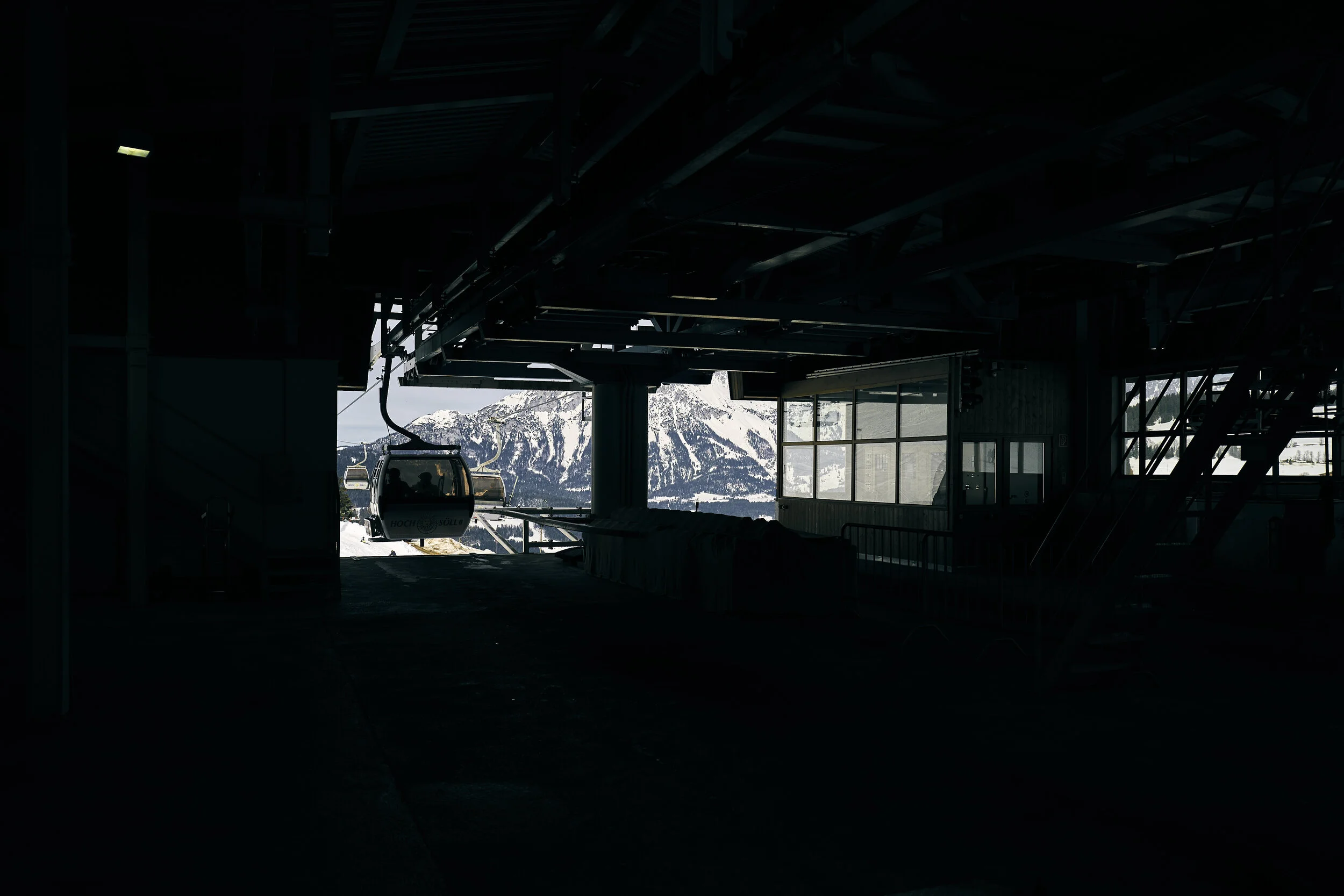 Seilbahnstation mit schneebedeckten Bergen im Hintergrund. Eine Gondelbahn verlässt die Station.