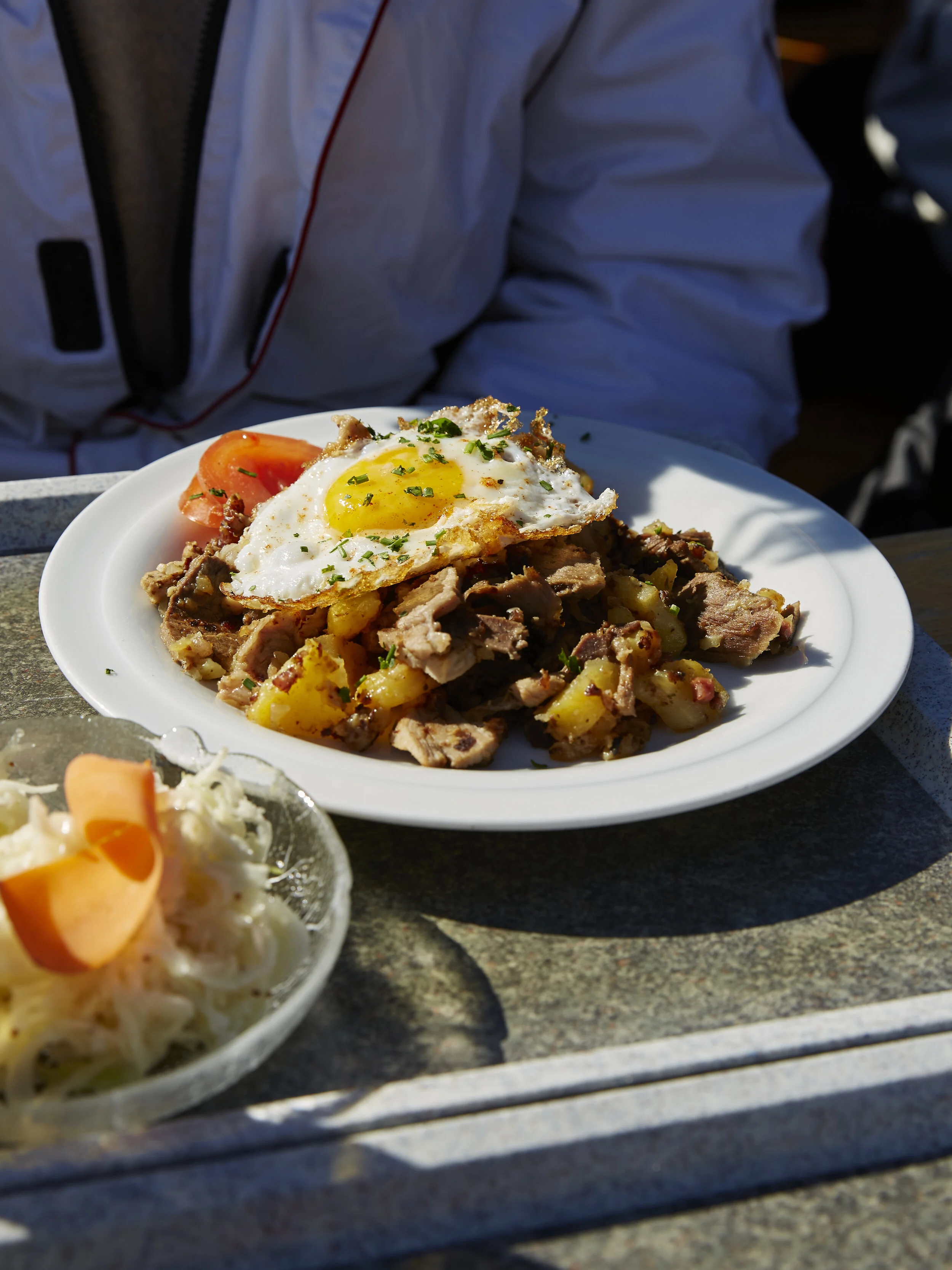 Teller mit Bratkartoffeln und gebratenem Ei, serviert mit einem Beilagensalat aus Kraut und Möhren.