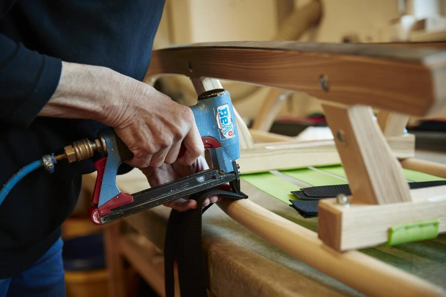 Person verwendet einen Heftgerät, um Stoff an einem Holzrahmen zu befestigen.