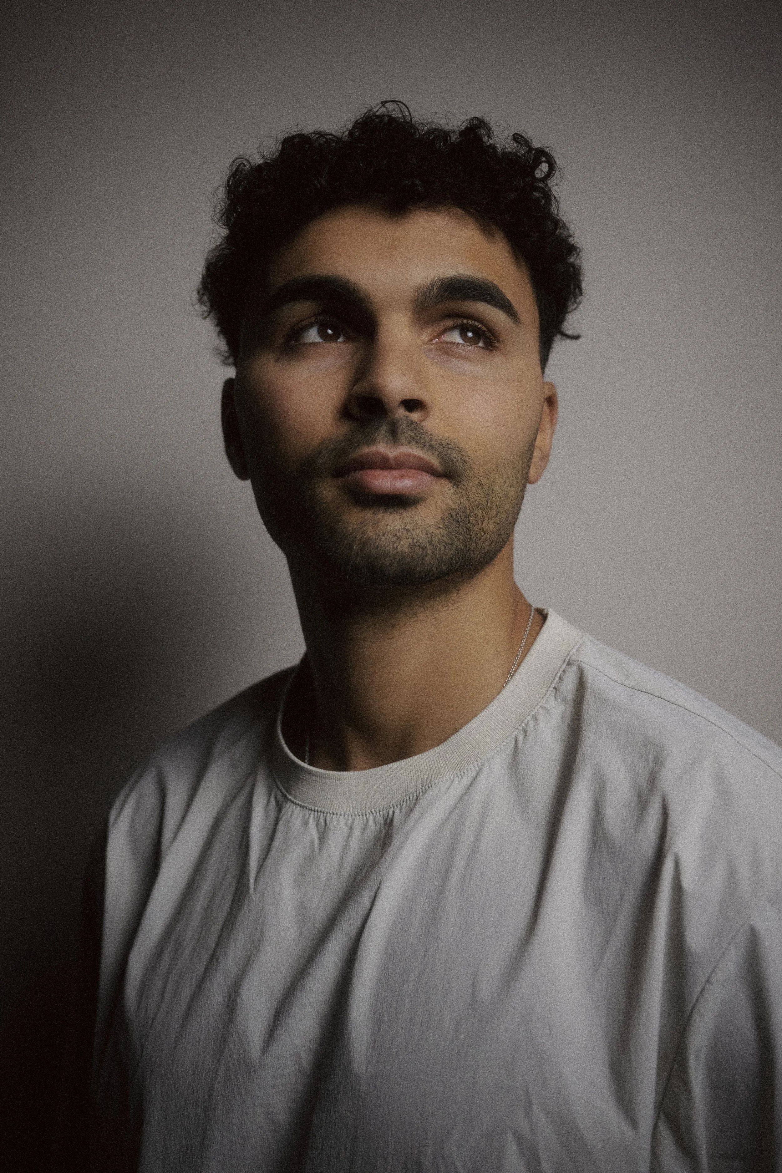 Porträt Younes Zarou, der nach oben schaut, vor einem grauen Hintergrund.