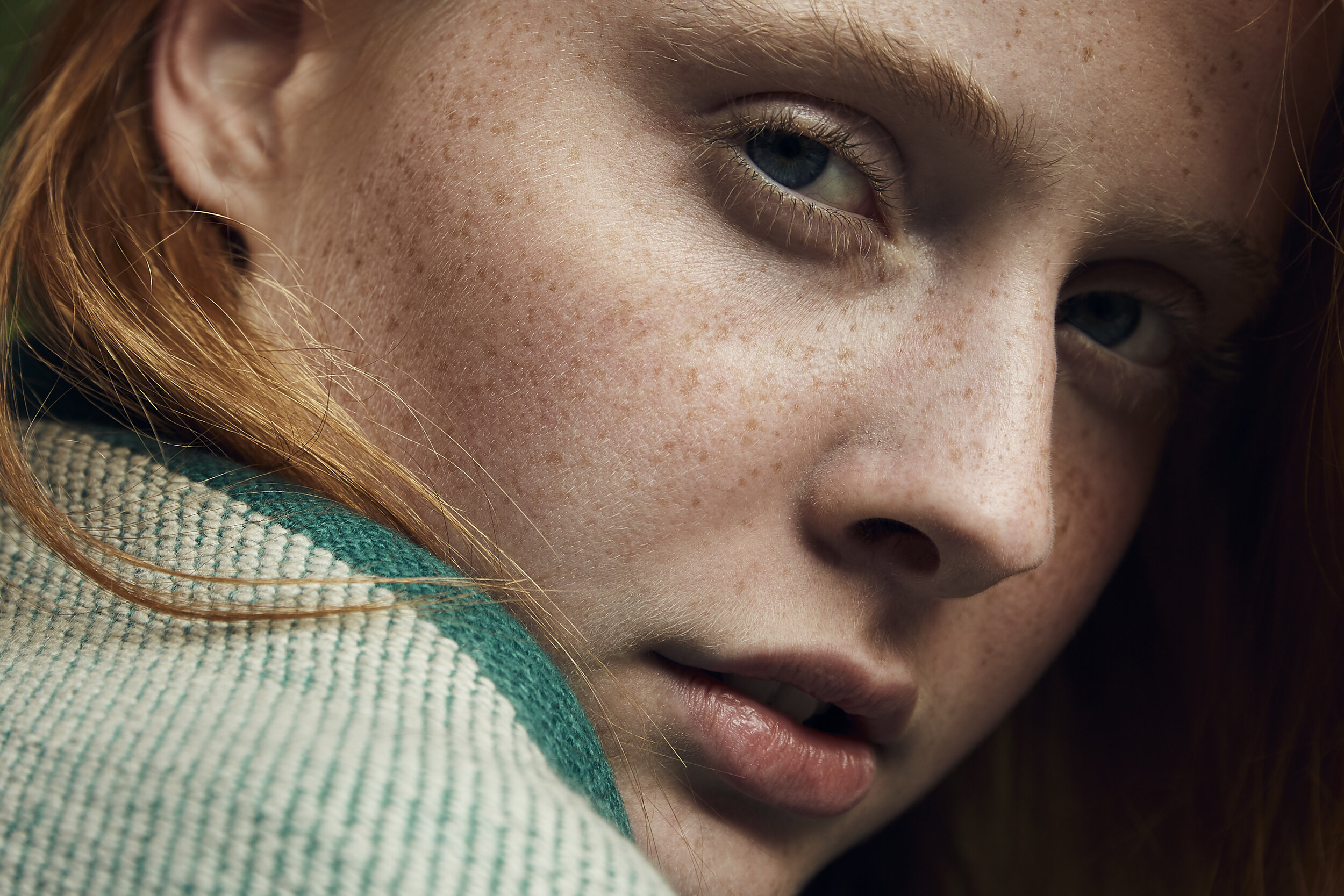 Nahaufnahme eines Gesichts mit Sommersprossen, roten Haaren und einem grünen Pullover.