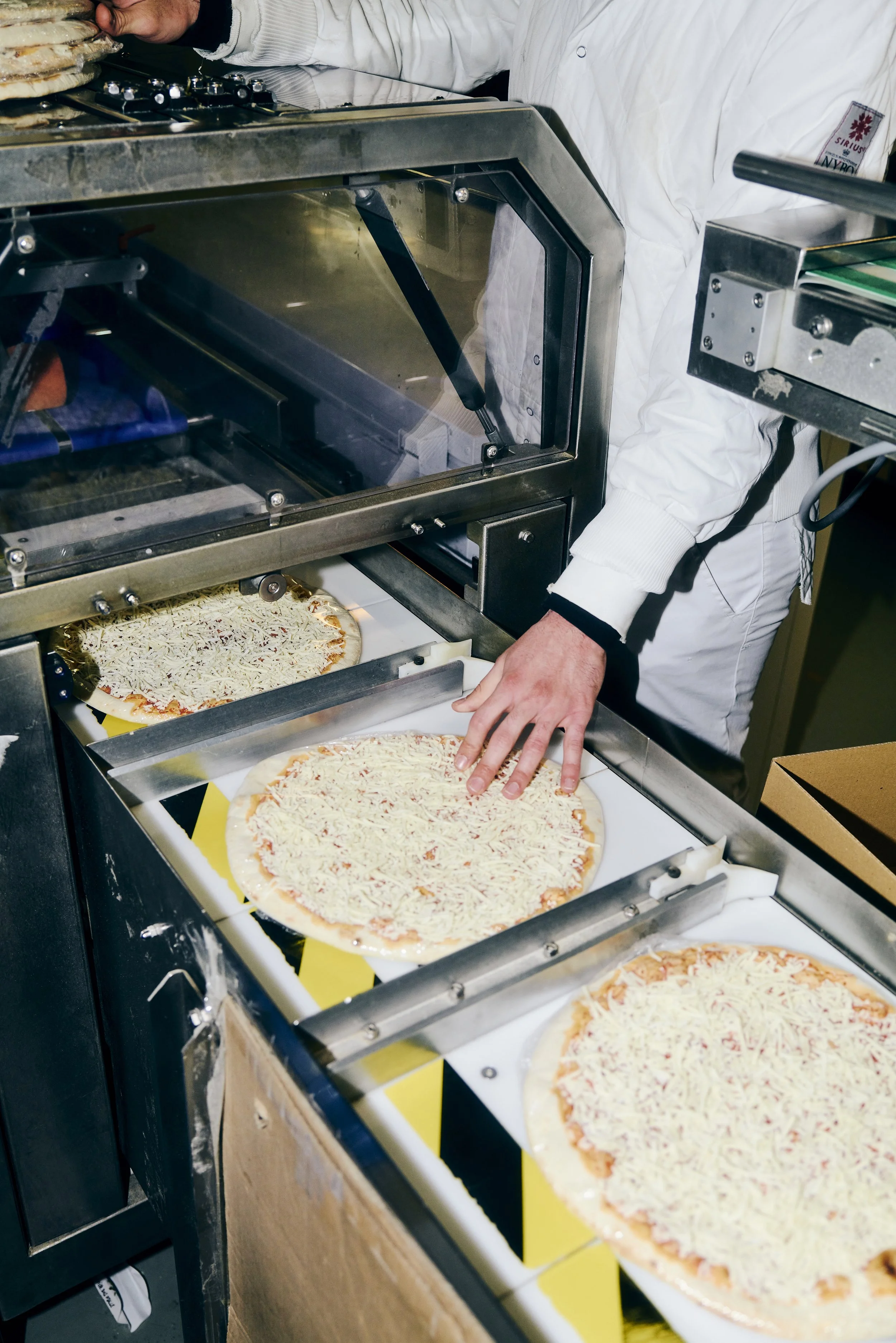 Ein Arbeiter in Schutzkleidung legt Pizzen auf ein Fließband in einer Fabrik.
