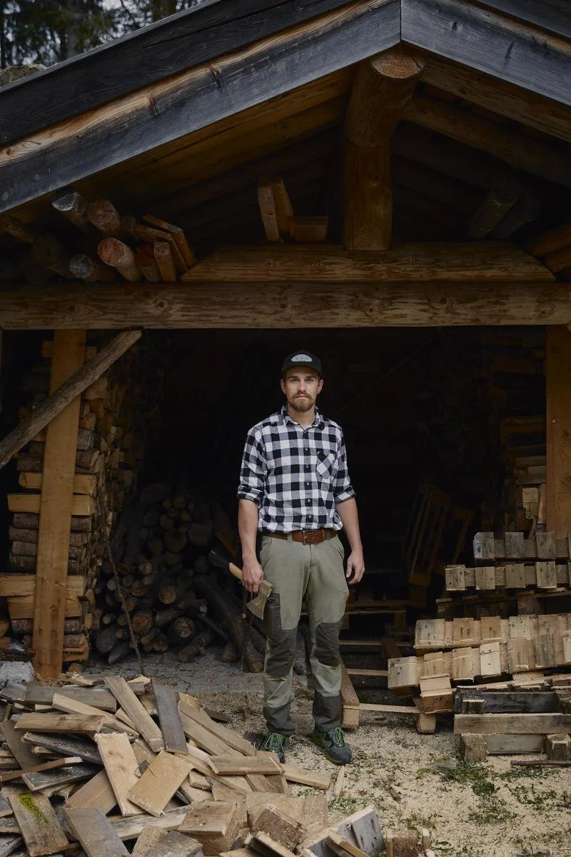 Mann mit Axt steht vor einem Holzschuppen.