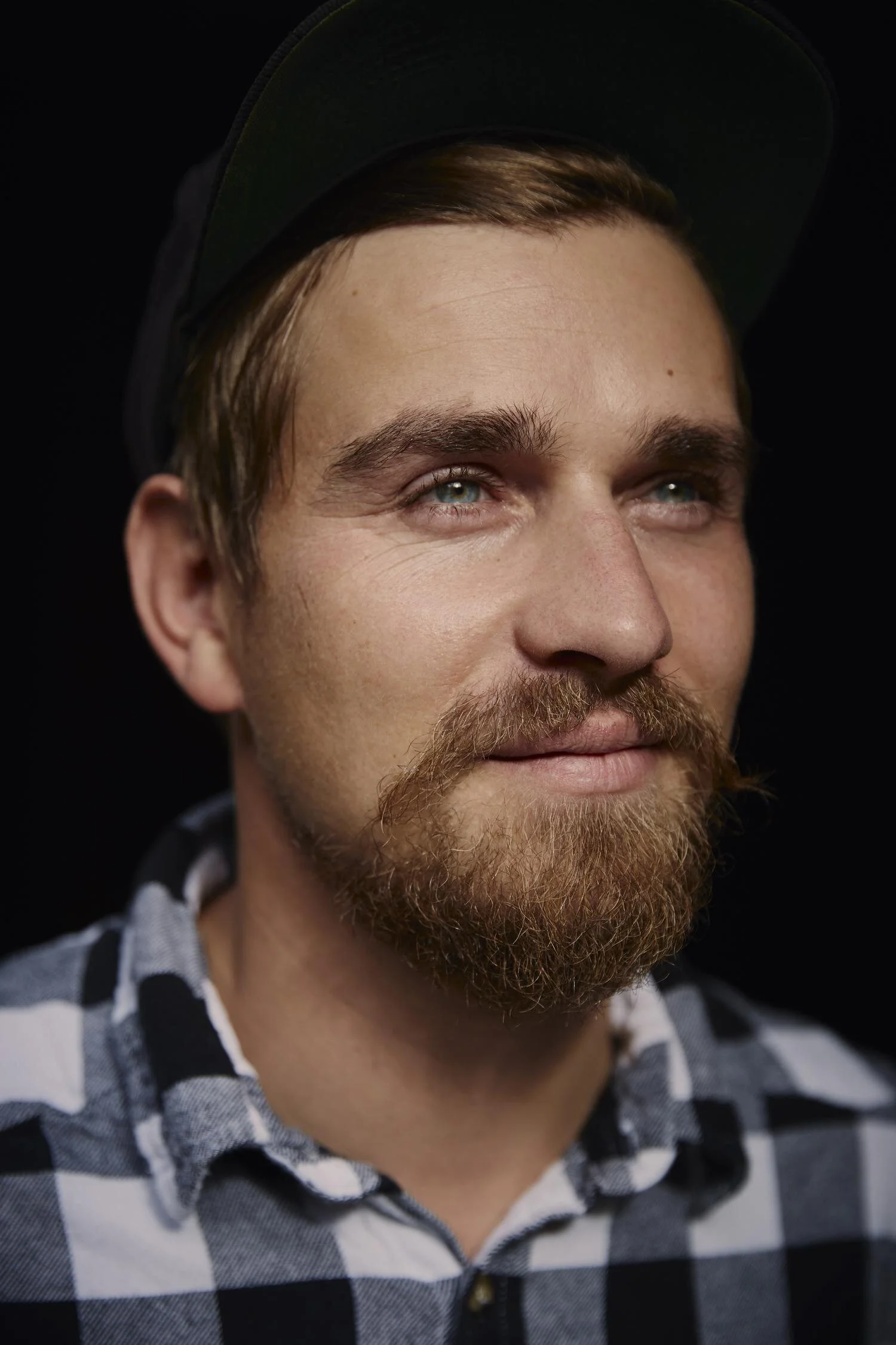 Porträt eines Mannes mit Bart und kariertem Hemd, der zur Seite schaut.