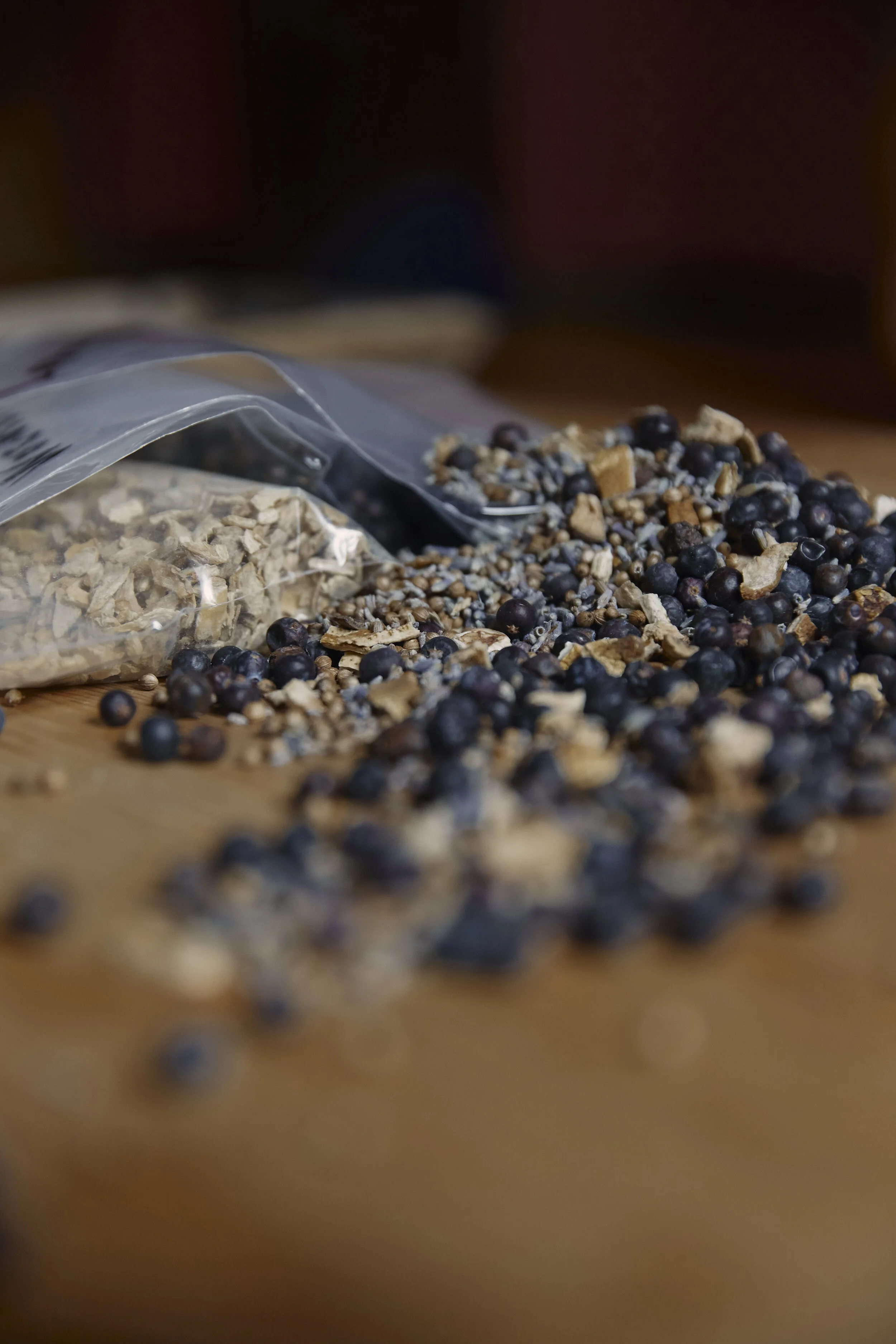 Tüte mit getrockneten Zutaten und Gewürzen auf einem Holztisch, mit verstreuten Beeren und Samen.