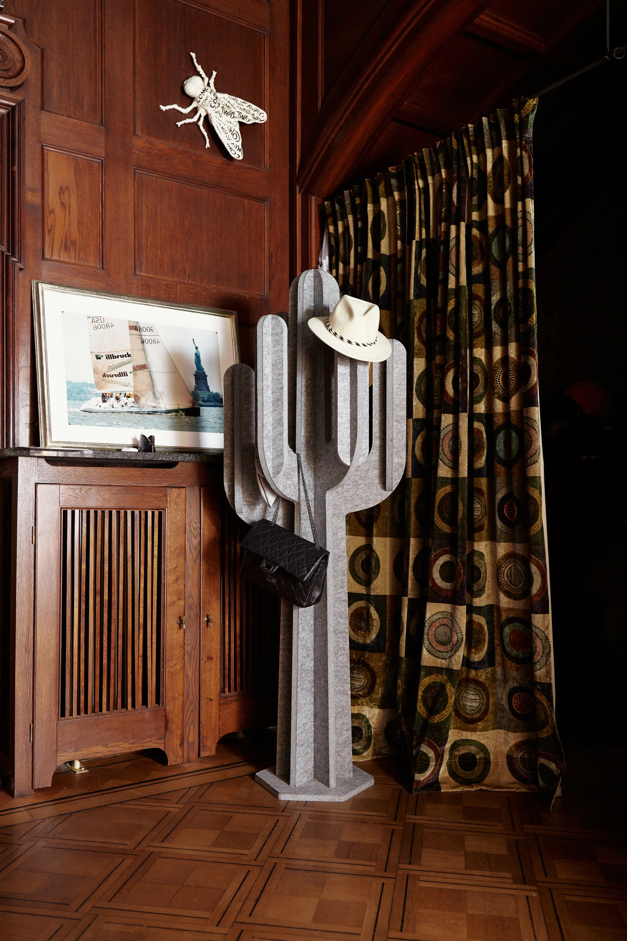 Innenraum mit Holzvertäfelung, grauer Kaktus-Kleiderständer mit Hut und Tasche, Bild von einer Segelboot-Szene, Vorhänge mit Rundmustern.
