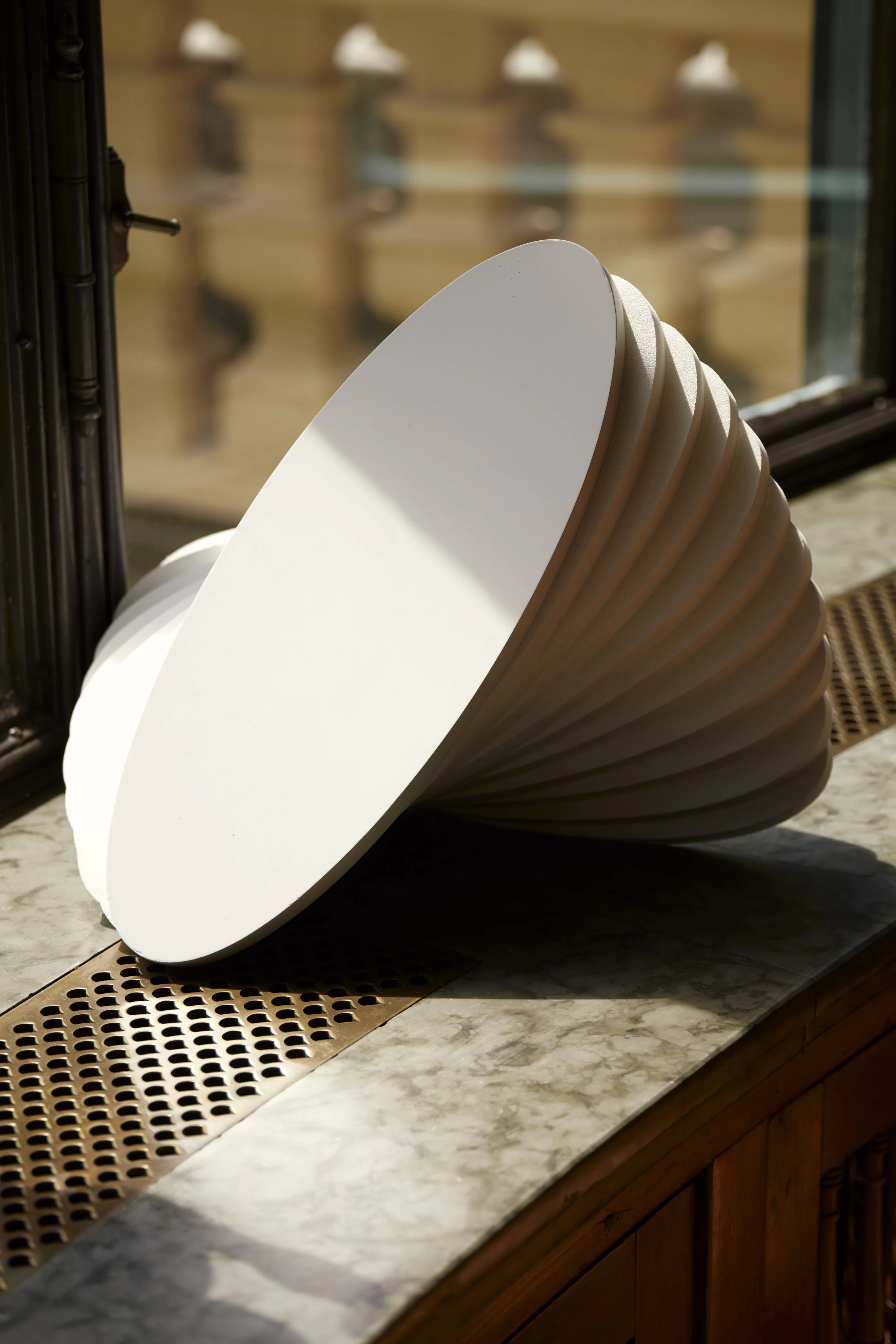 Modernes weißes, gerilltes Objekt auf einer Fensterbank aus Marmor.