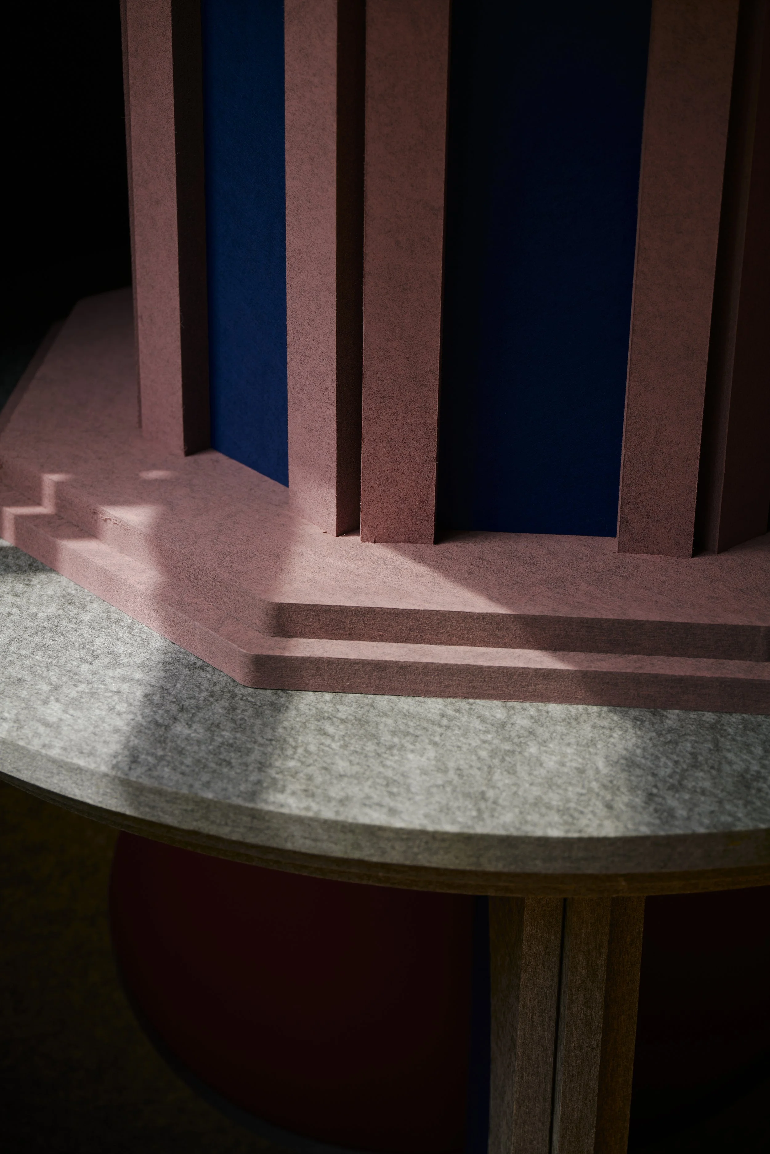 Nahaufnahme einer strukturierten, architektonisch aussehenden Konstruktion aus rosafarbenem, blauem und grauem Material mit Licht- und Schatteneffekten.