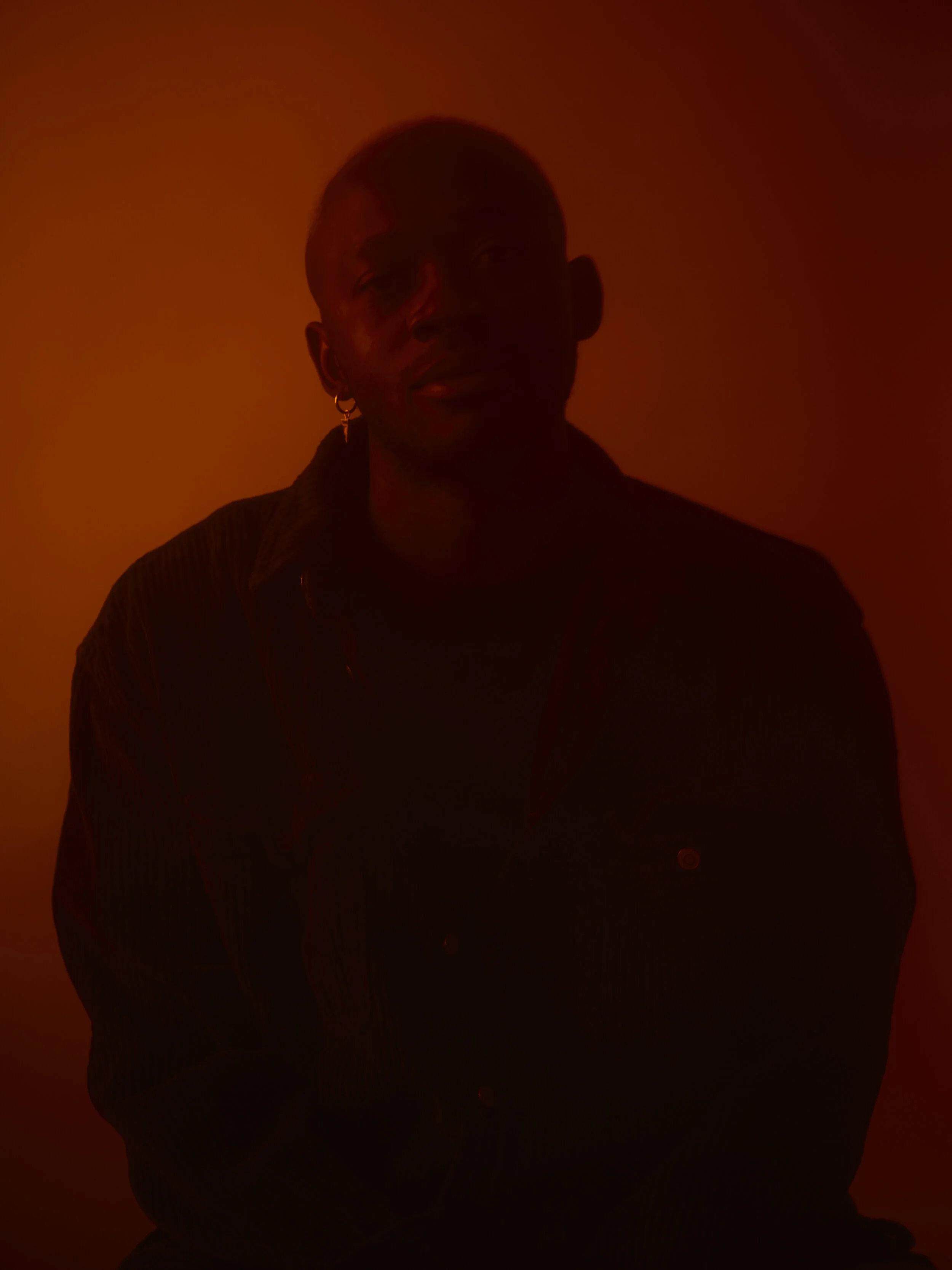 Ein Porträt eines Mannes in dunkler Beleuchtung mit einem warmen, orangefarbenen Hintergrund.