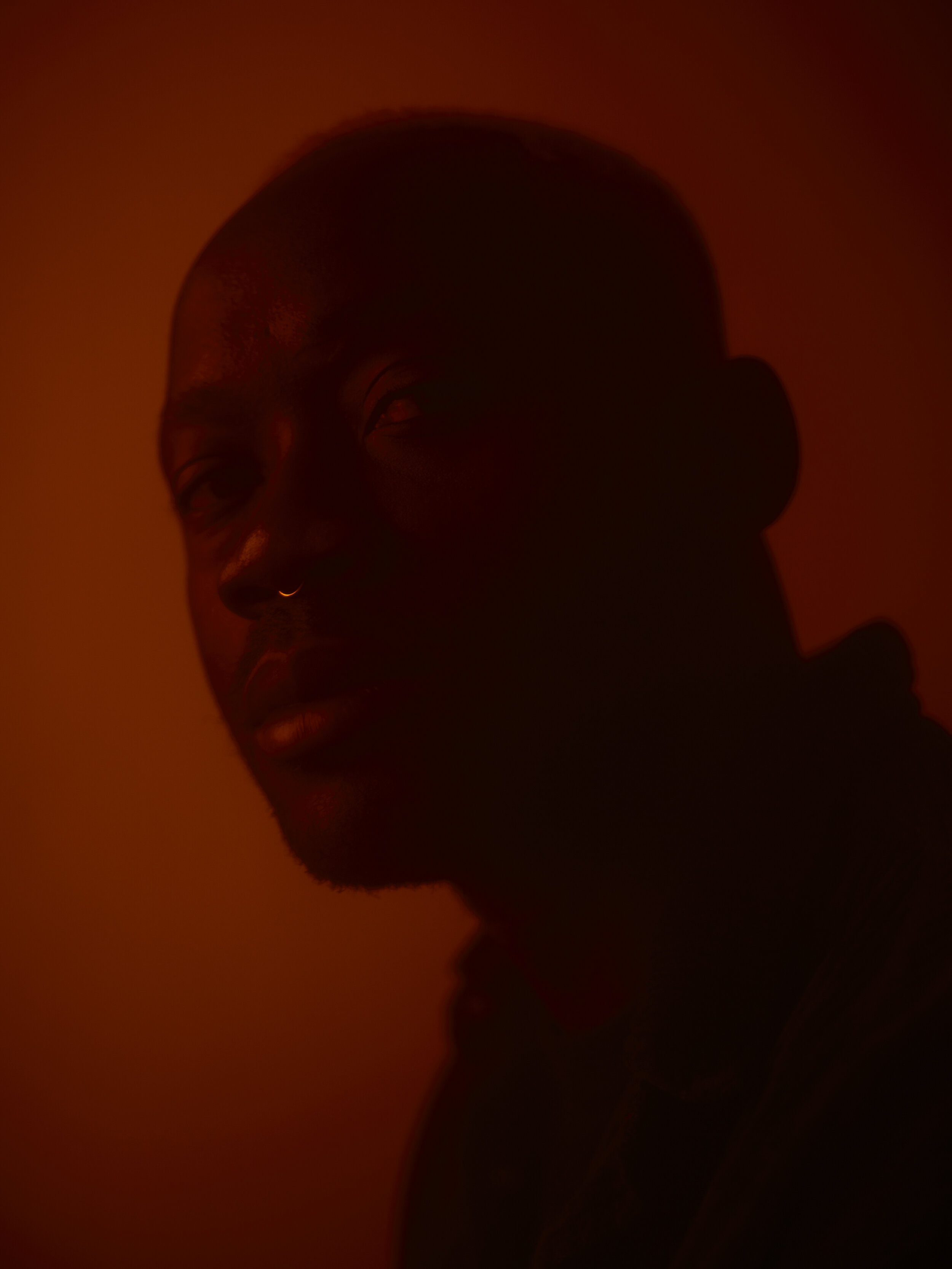 Schattenhaftes Porträt eines Mannes mit Nasenpiercing in dunklen, orangefarbenen Licht.