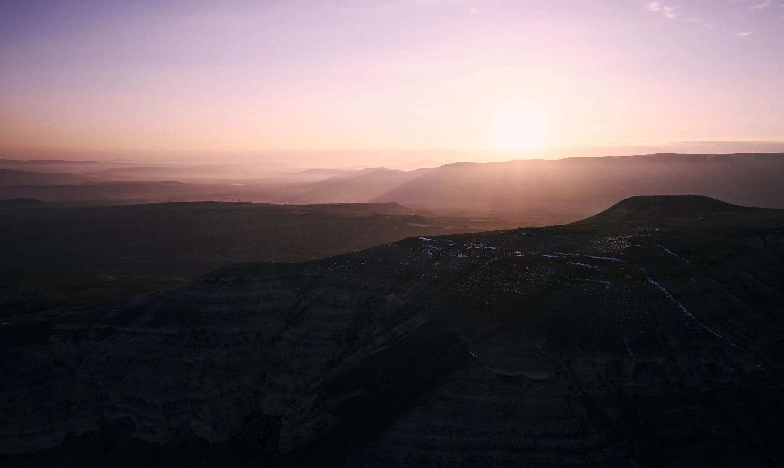 Sonnenaufgang über einer Berglandschaft mit weiten Hügeln und Tälern im Hintergrund. Der Himmel ist lila und orangefarben.