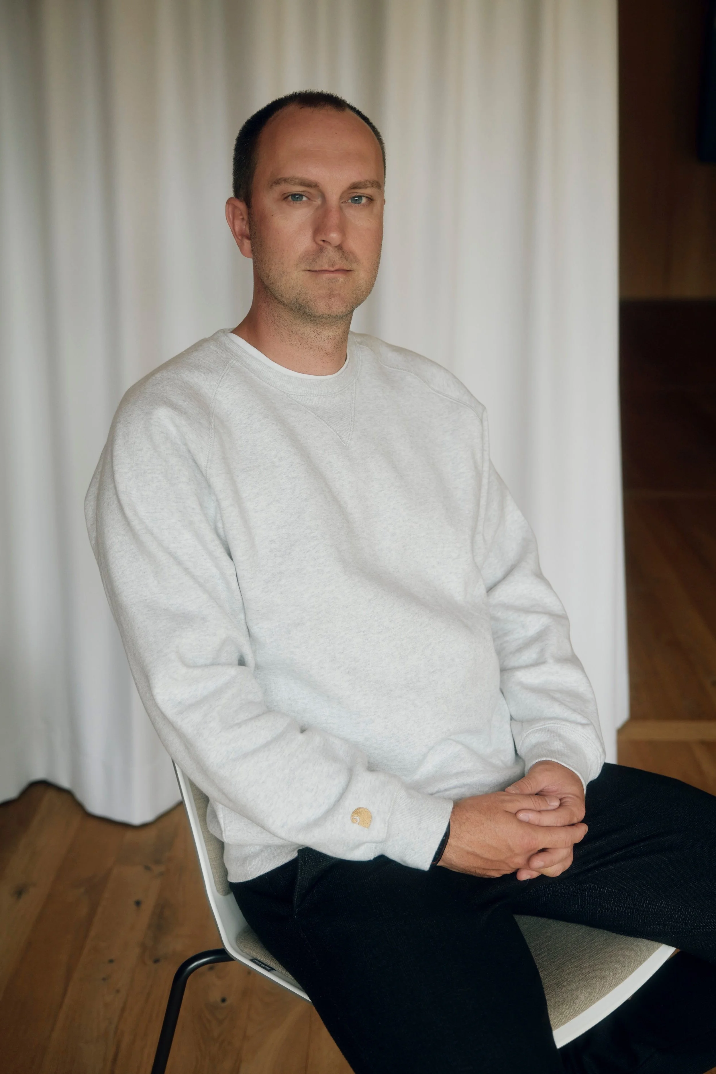 Ole Werner sitzt auf einem Stuhl vor einem hellen Vorhang. Er trägt ein hellgraues Sweatshirt und schwarze Hosen.