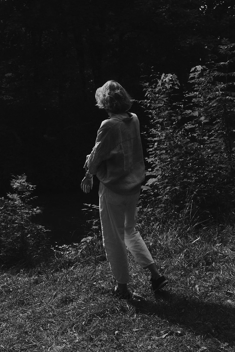 Schwarz-Weiß-Foto einer Person im Freien, die von hinten gezeigt wird, umgeben von Bäumen und Pflanzen.
