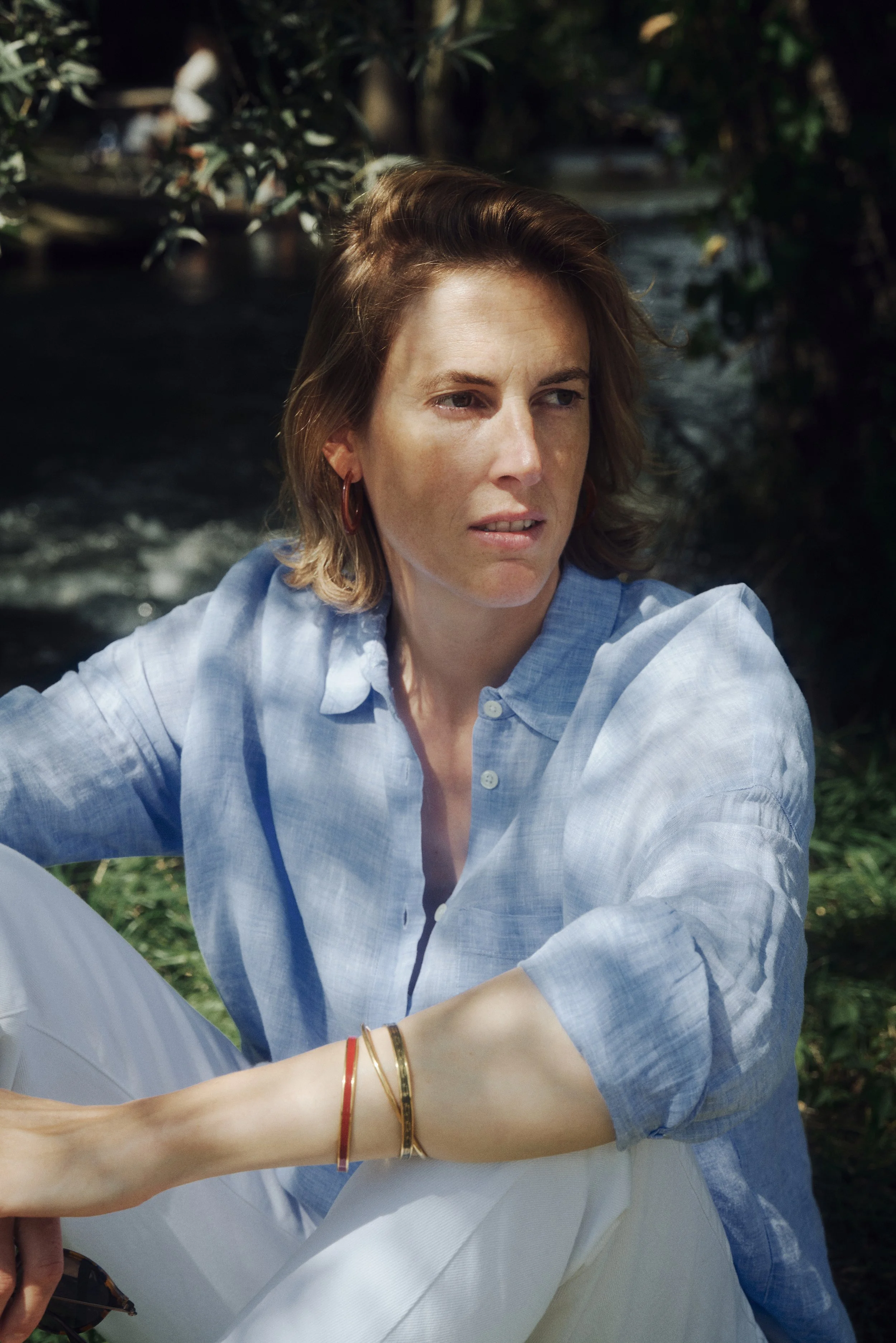 Isabelle Rickmers in blauer Bluse sitzt im Freien, nahe einem Fluss, umgeben von Grün.