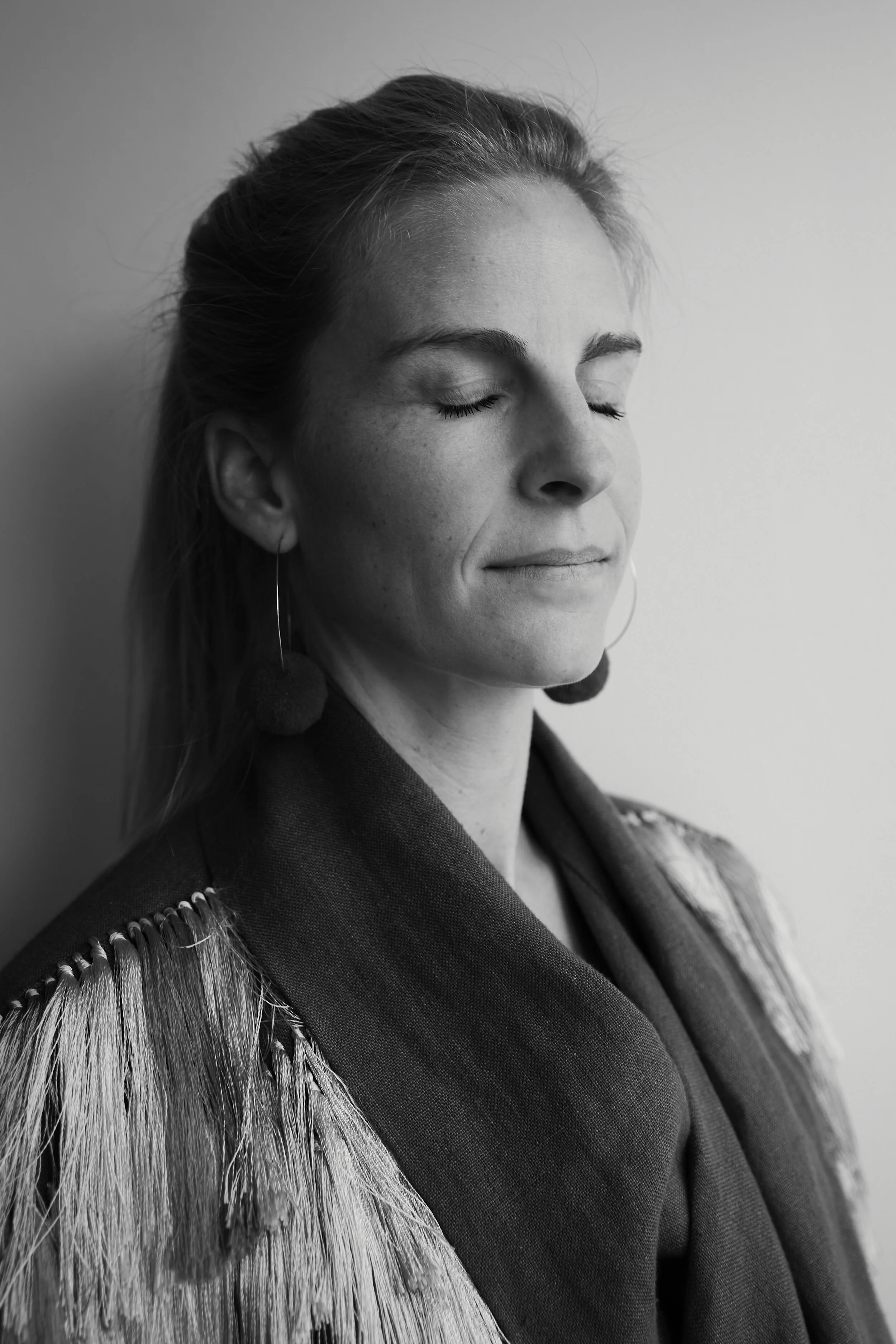 Schwarzweiß-Bild einer Frau mit geschlossenen Augen, die seitwärts posiert. Sie trägt einen Schal und hat lange Ohrringe. Die Frau wirkt entspannt.