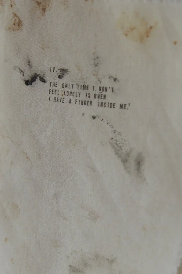 Text auf Stoff mit Flecken und Handabdrücken. Der Text lautet: 'IV. The only time I don't feel lonely is when I have a finger inside me.'