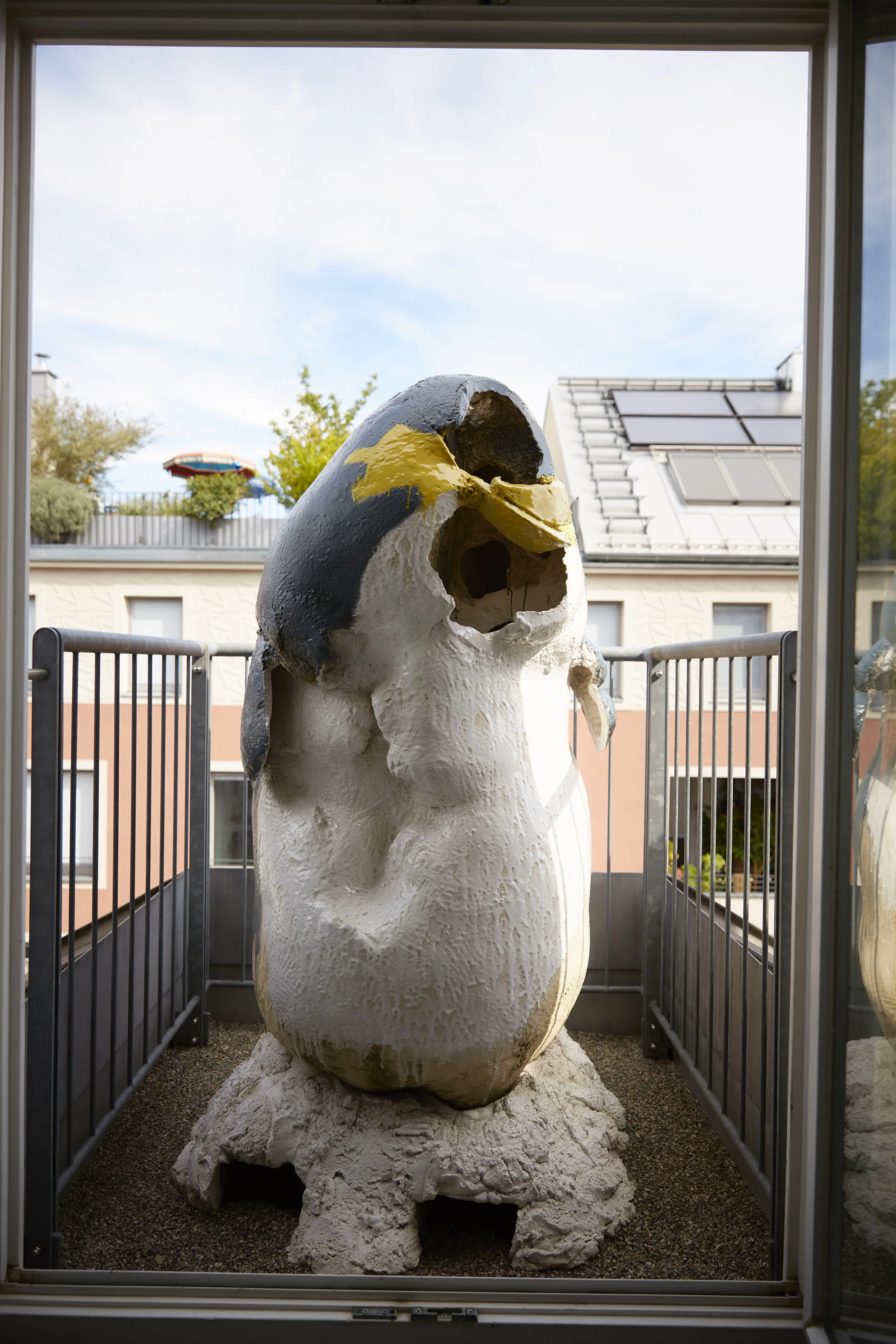 Große Pinguin-Skulptur auf einem Balkon vor städtischem Hintergrund.