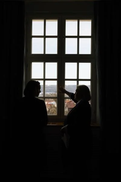 Schatten von zwei Personen, die vor einem Fenster stehen und sich unterhalten. Eine Person zeigt durch das Fenster nach draußen.