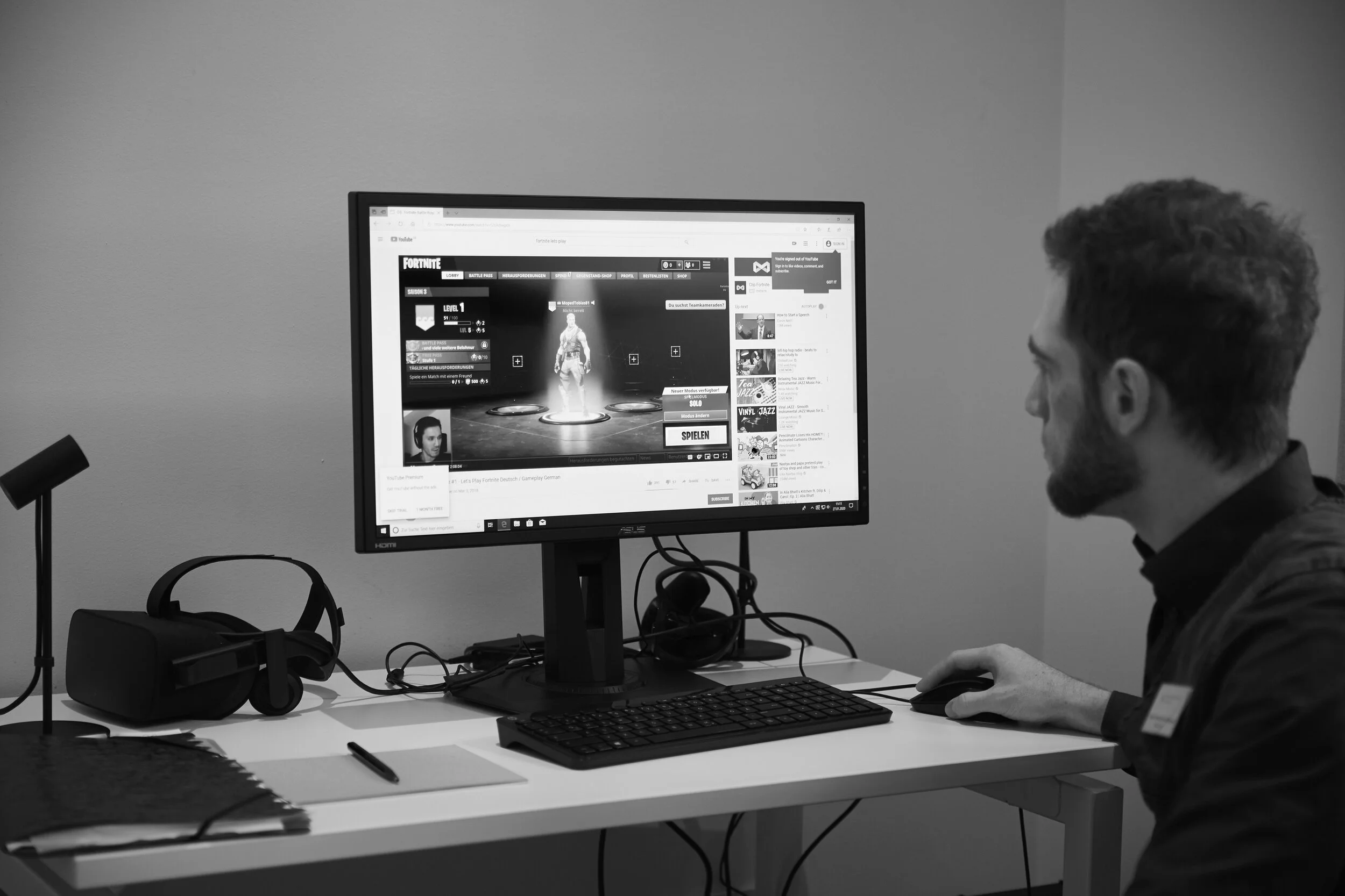 Person spielt Fortnite auf einem Computer mit Kopfhörern und VR-Headset auf dem Tisch.