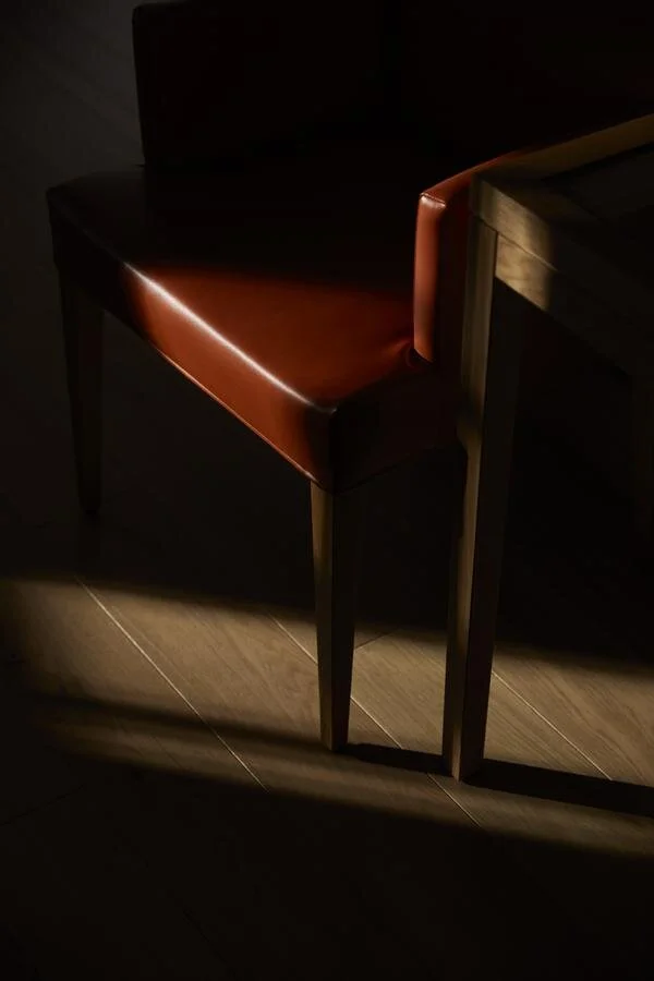 Holzstuhl mit brauner Lederpolsterung, beleuchtet durch Sonnenlicht auf Holzboden.