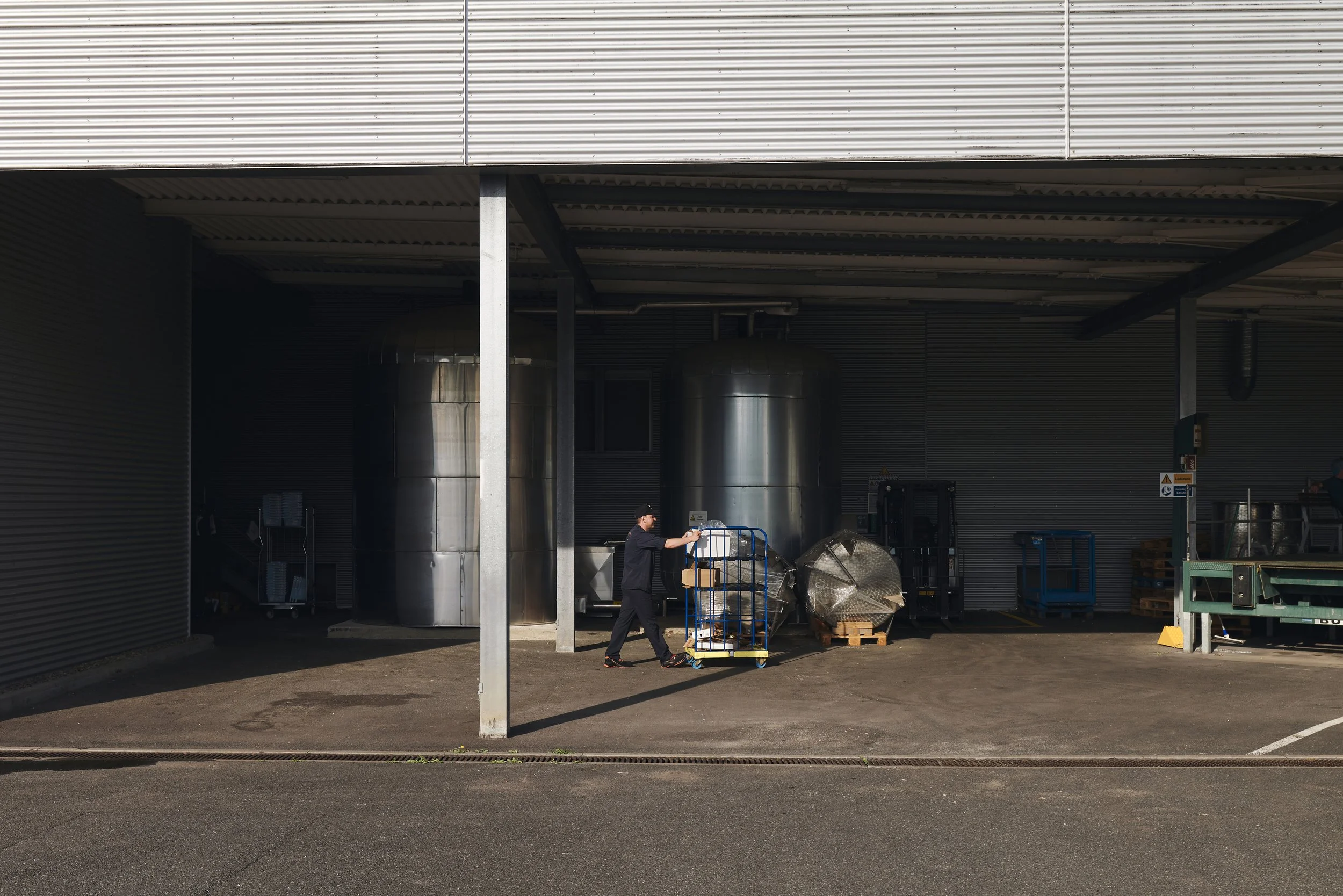 Lagerbereich mit Metalltanks, ein Mann schiebt einen Wagen mit Kisten.