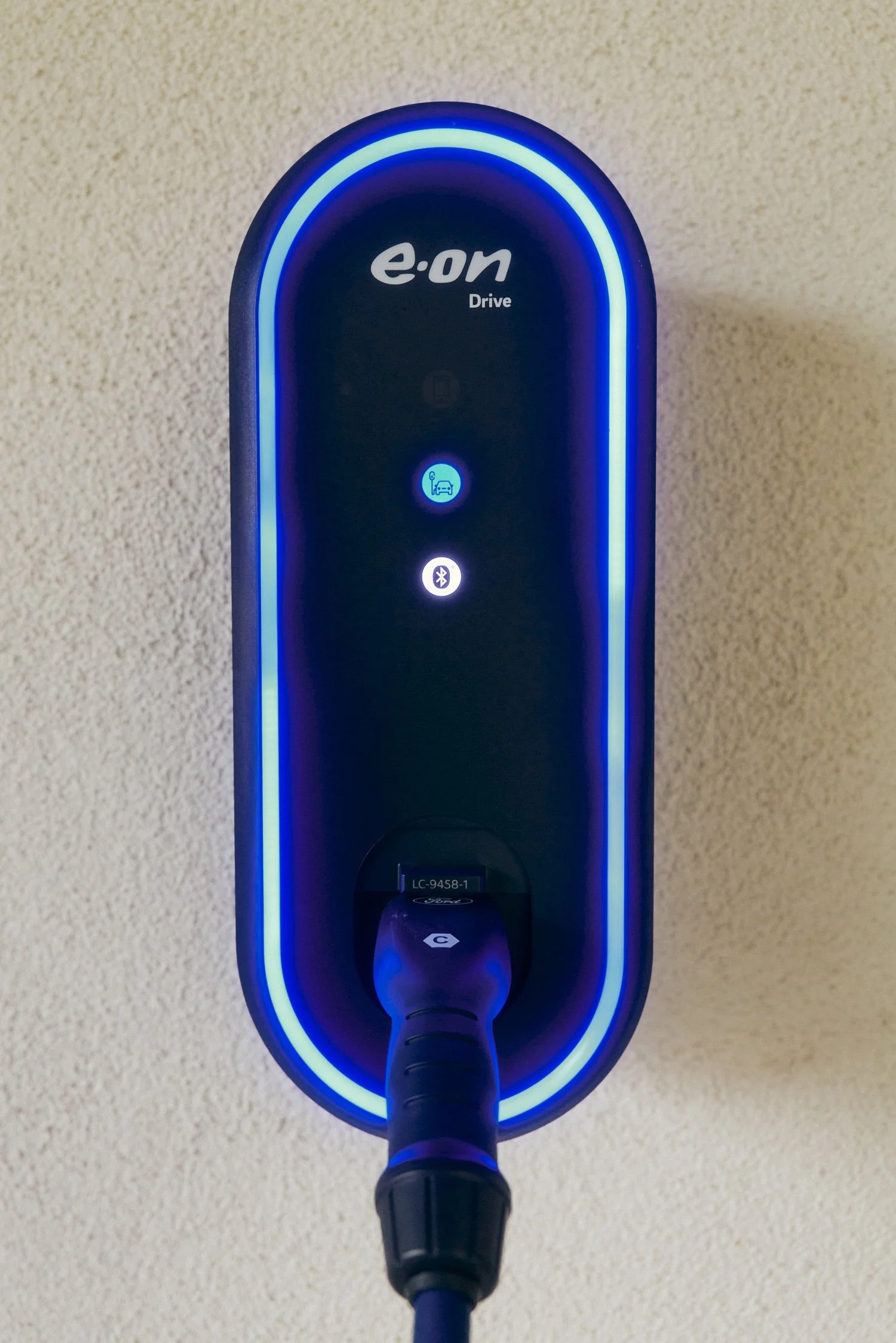 Ladestation für Elektrofahrzeuge mit blau beleuchtetem Rand an einer beige Wand montiert, Marke "e.on Drive" sichtbar.
