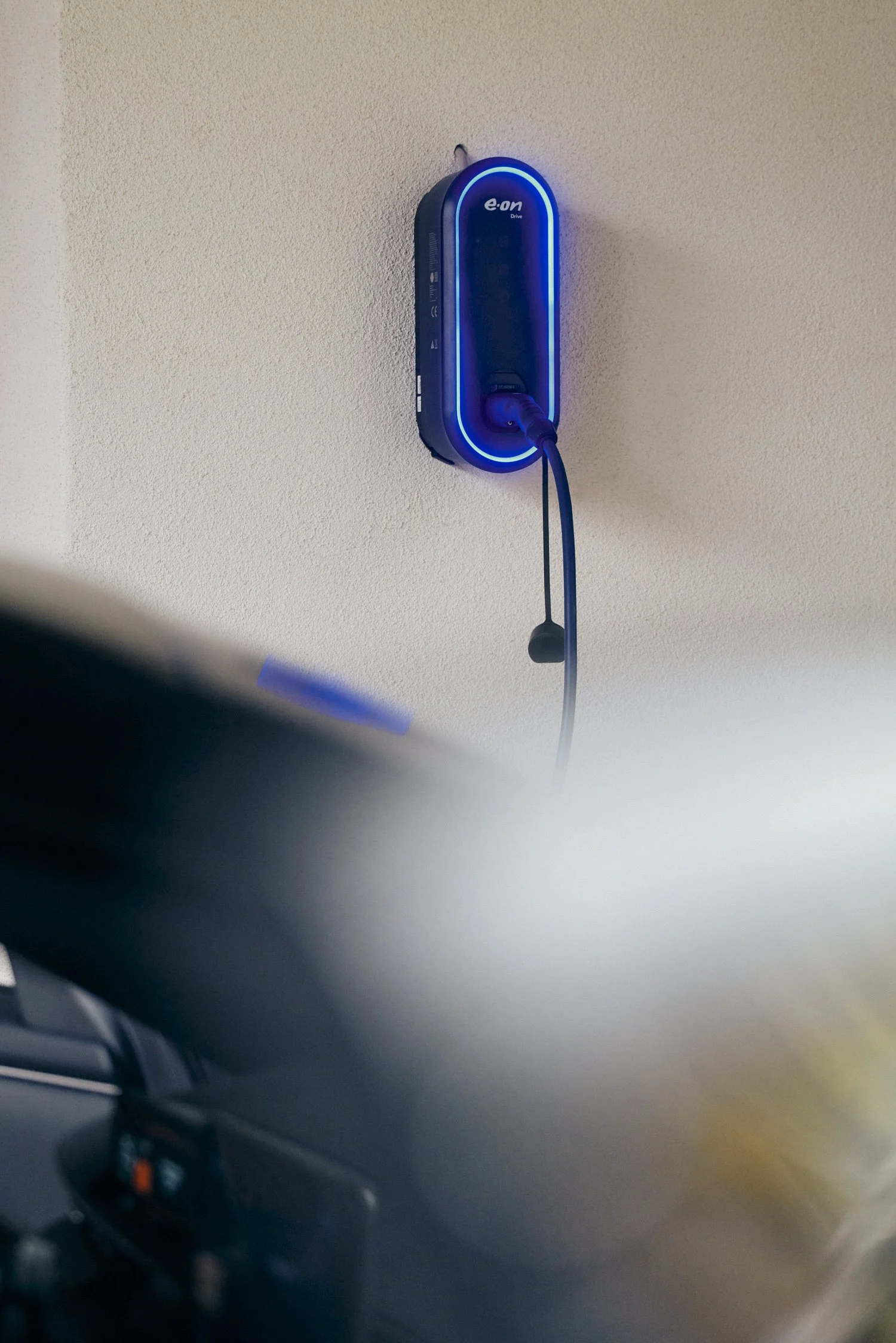 Wandladestation mit blauem Leuchtring, an der ein Ladekabel angeschlossen ist.