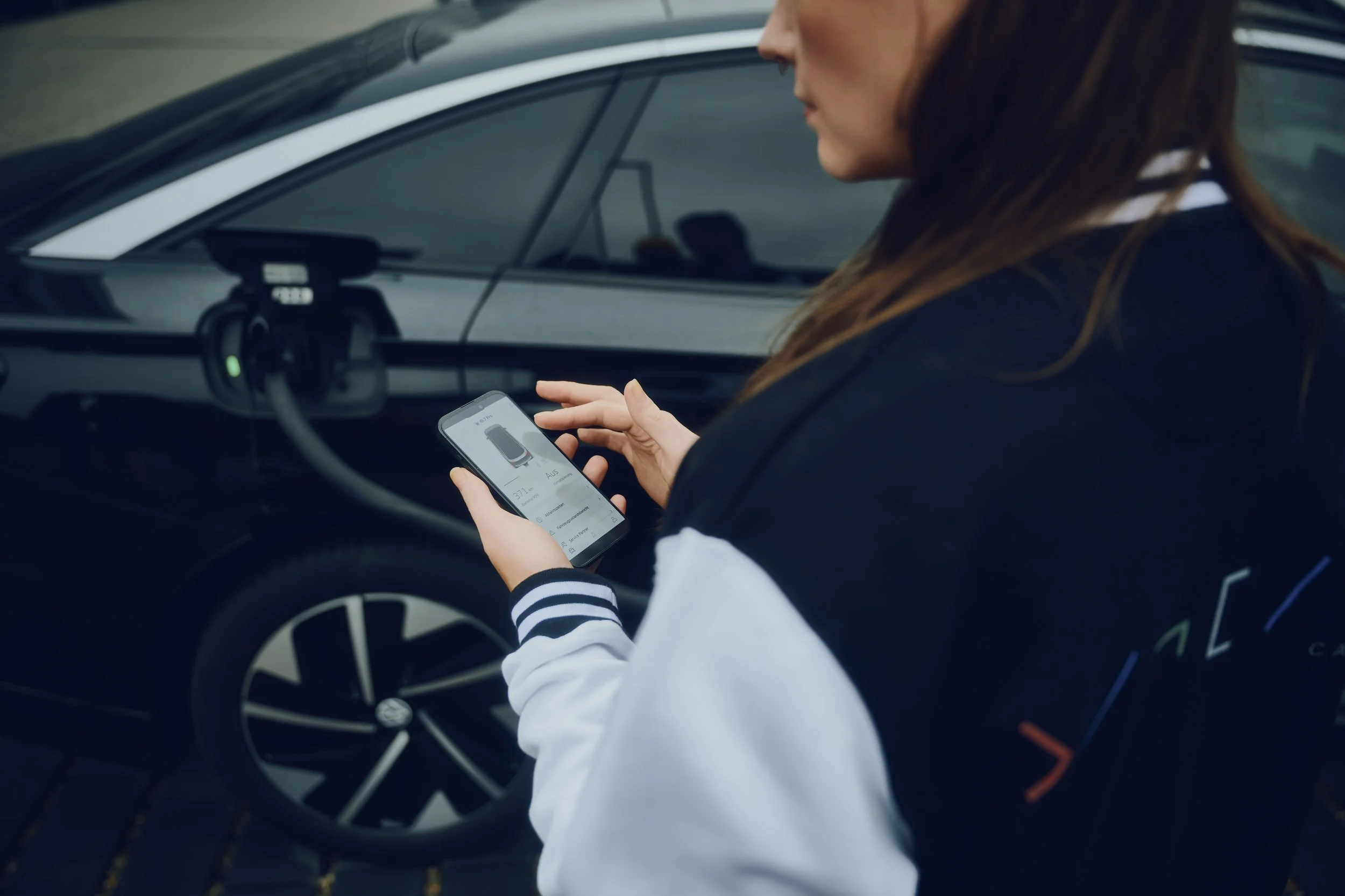 Eine Person benutzt ein Smartphone, während ein Elektroauto aufgeladen wird.