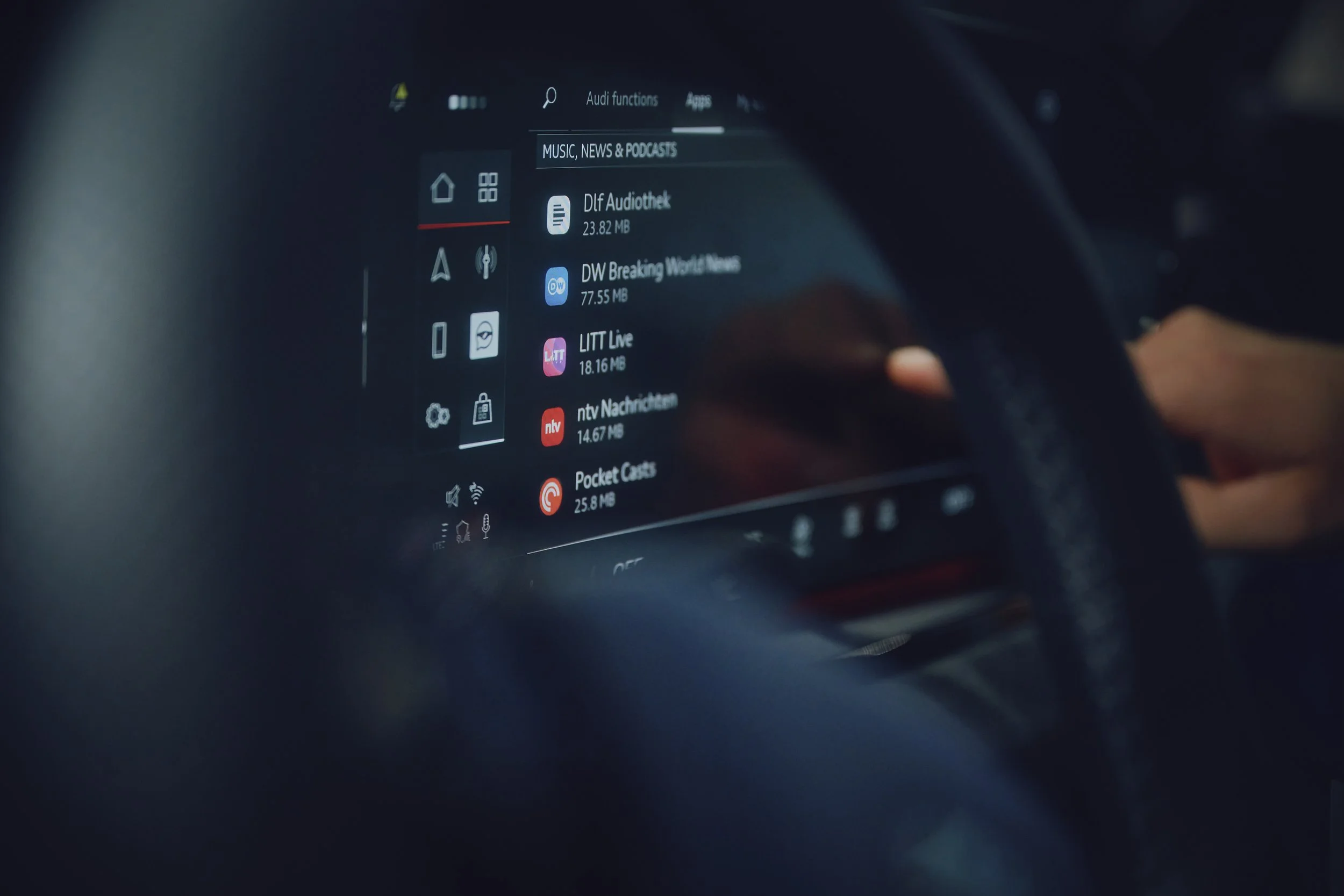 Nahaufnahme eines Auto-Infotainmentsystems, das verschiedene Medien-Apps und Nachrichtenquellen auf einem Touchscreen anzeigt. Eine Hand interagiert mit dem Display.