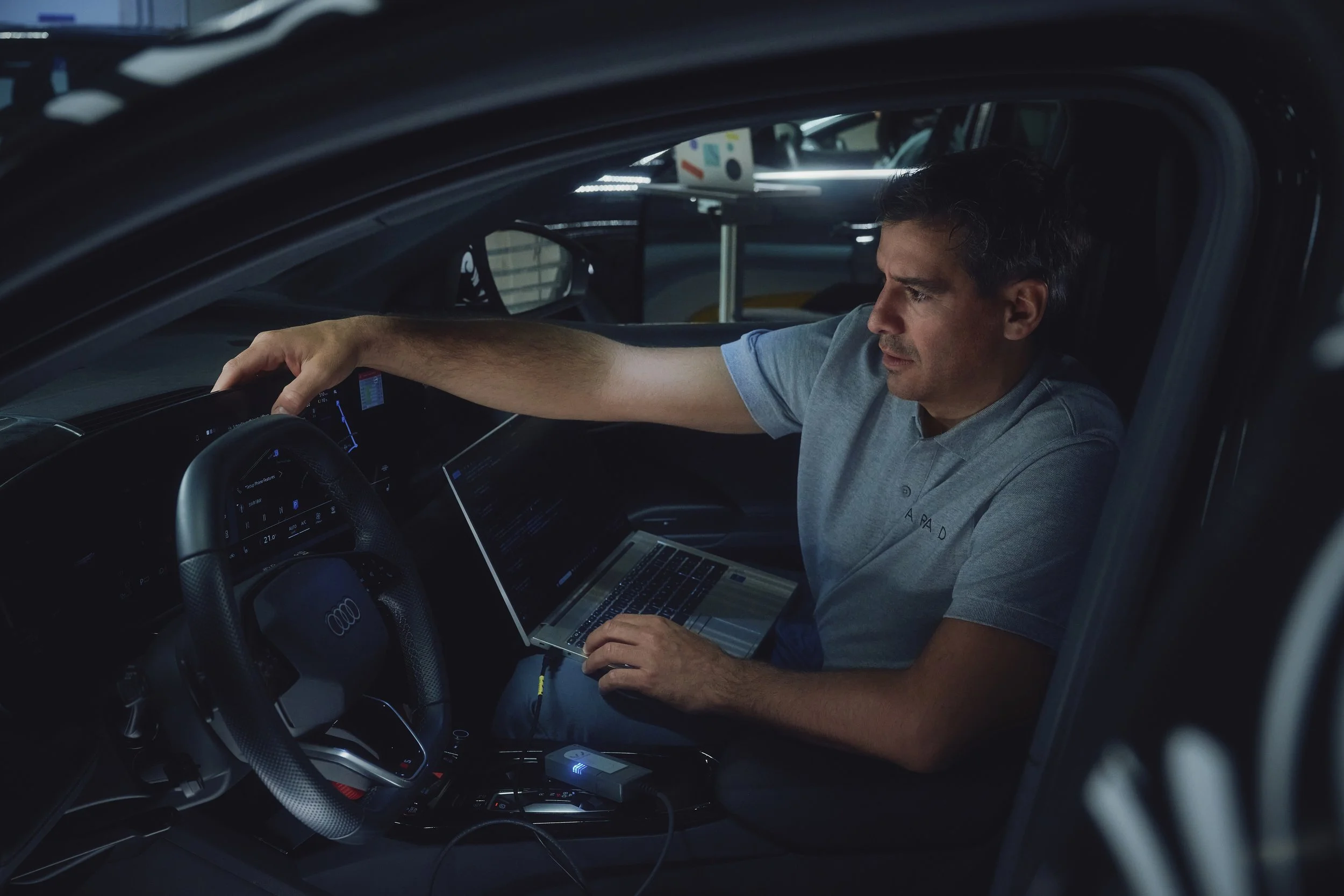 Mann sitzt im Auto, arbeitet mit einem Laptop.