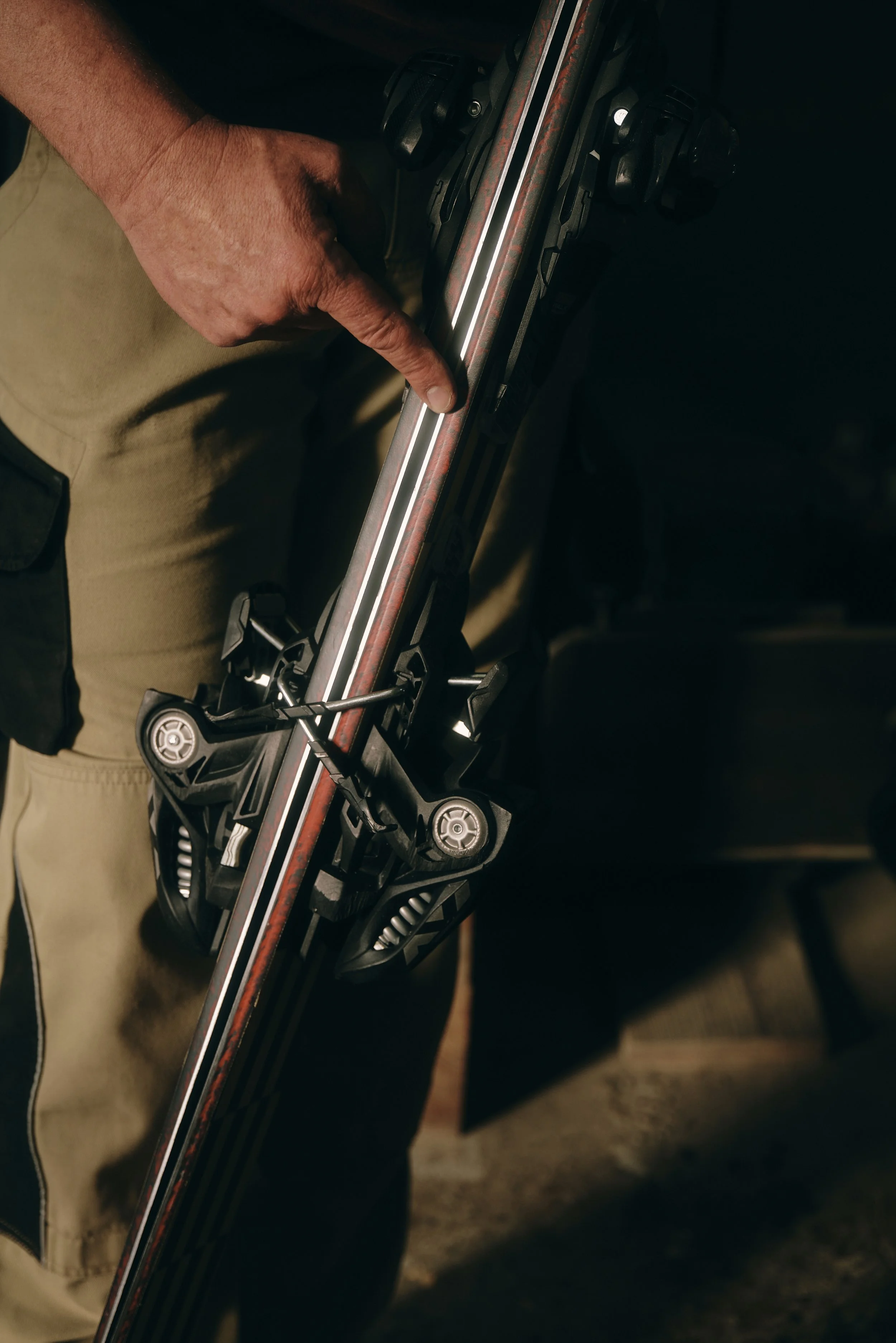 Nahaufnahme einer Hand, die auf einen Ski mit Bindung zeigt.