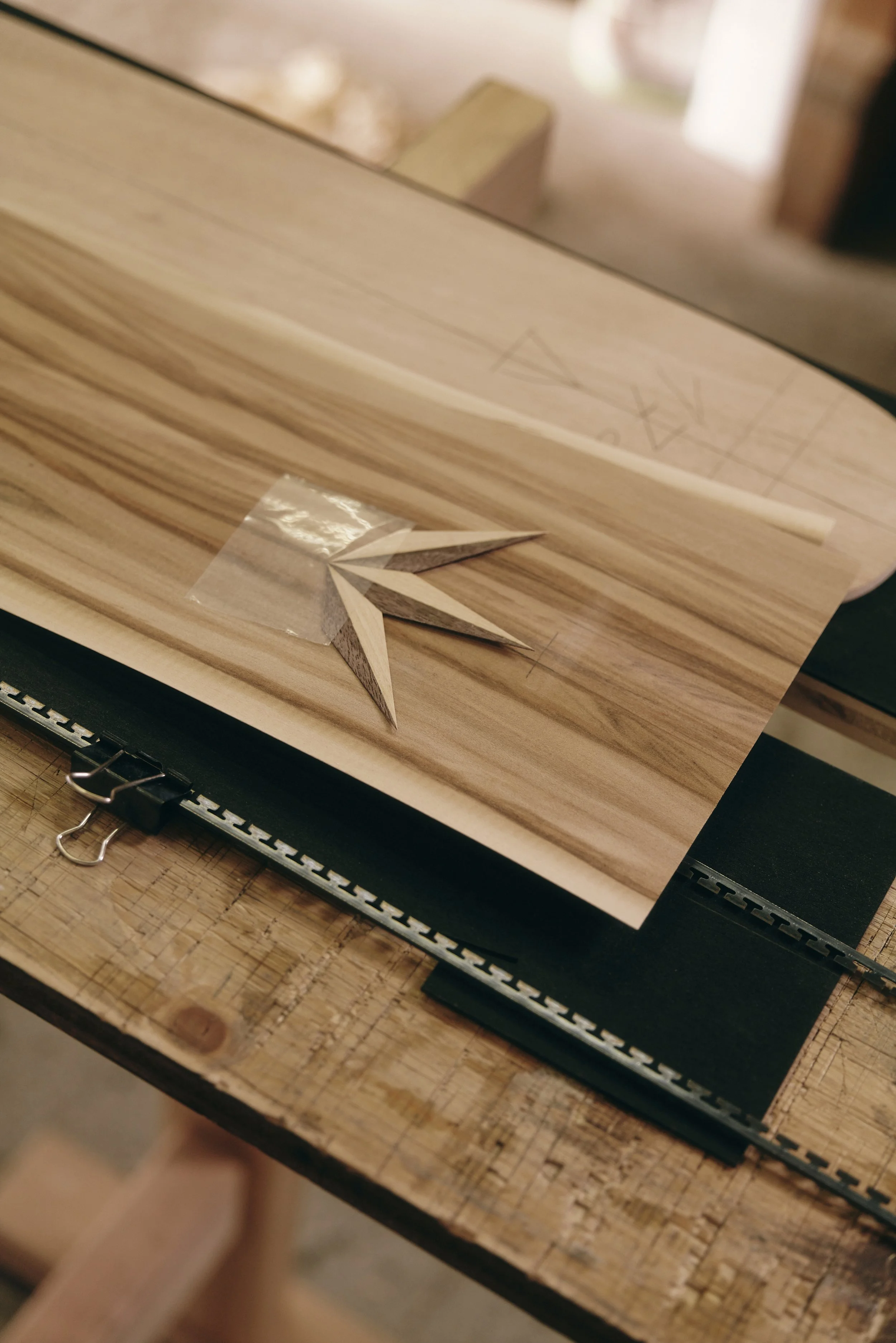 Nahaufnahme eines Holztisches mit Holzfurnierblättern und Dekor im geometrischen Muster, befestigt mit einer Papierklemme.