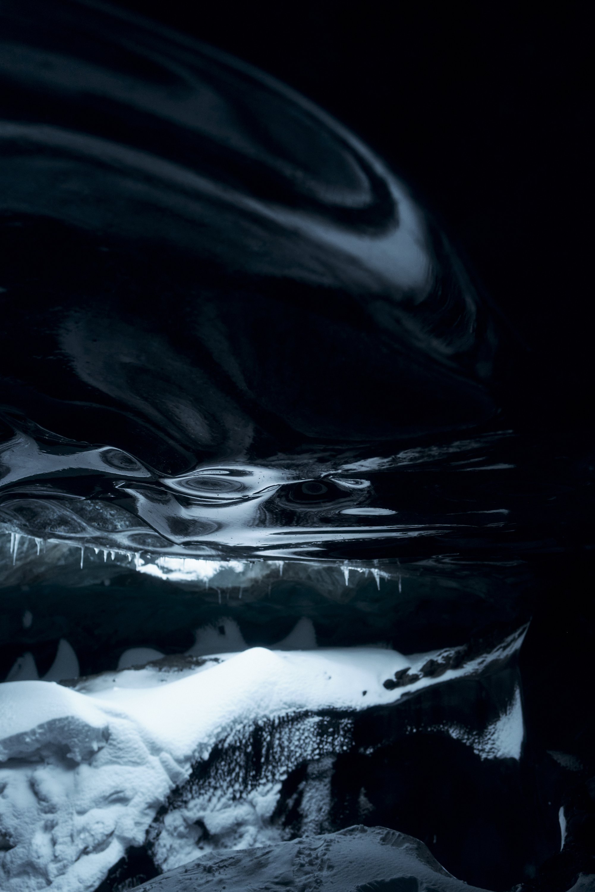 Innenseite einer Eishöhle mit Eisformationen und dunklen, glatten Wänden, stimmungsvolles Licht.