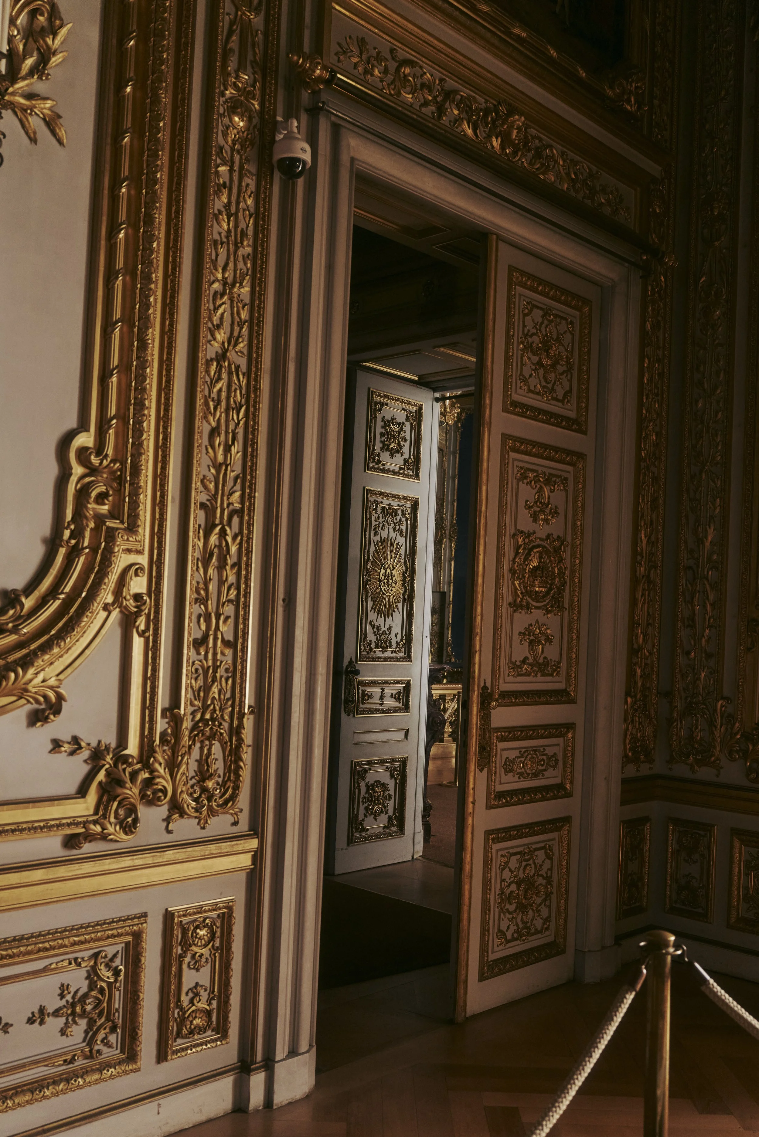 Prunkvoll verzierter Raum mit goldenen Details, geöffnete Tür zeigt ein weiteres ähnlich gestaltetes Zimmer, Dekoration reich verziert, klassische Eleganz.