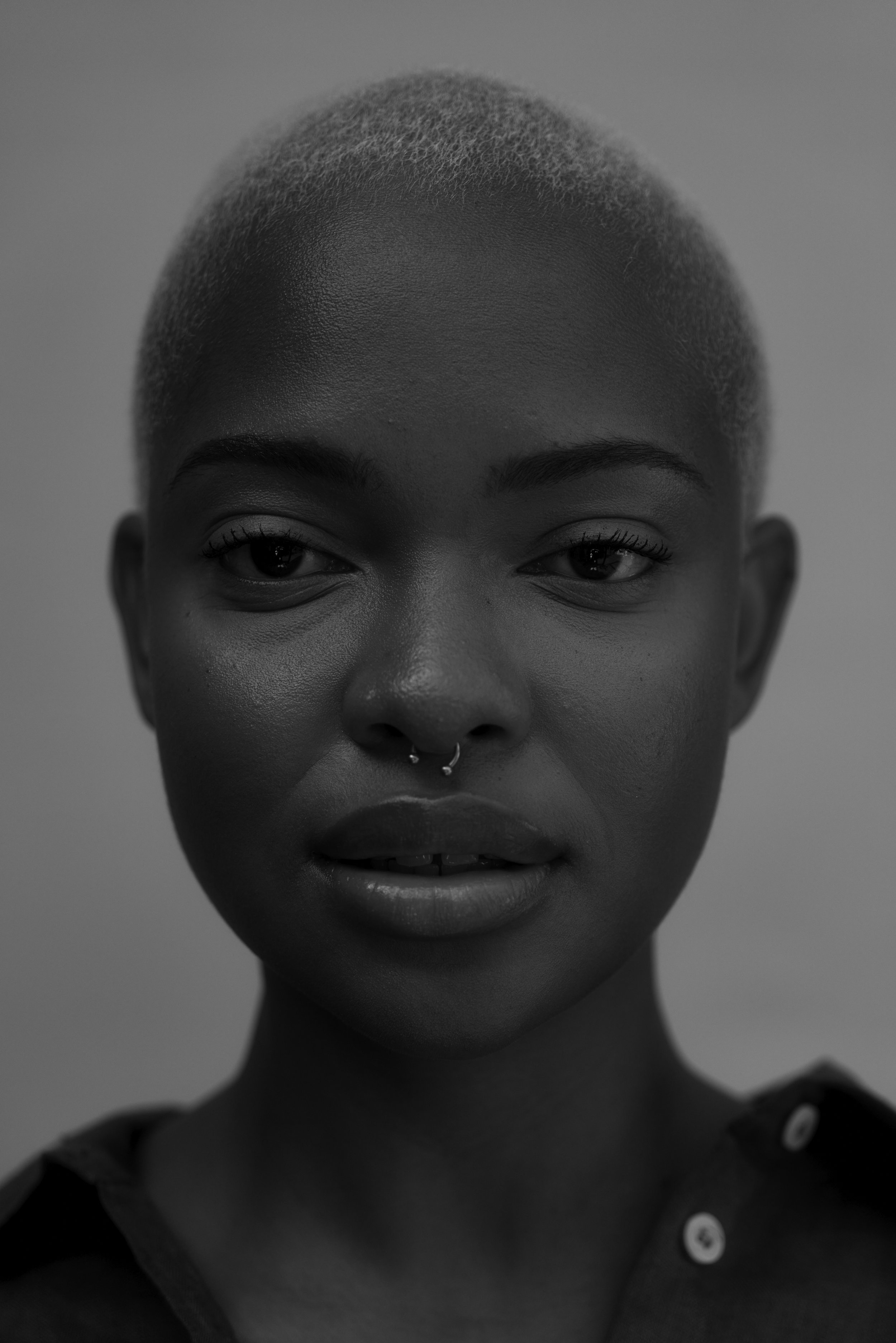 Nahaufnahme einer Person mit kurzem, krausem Haar und Nasenpiercing. Schwarzweiß-Fotografie.
