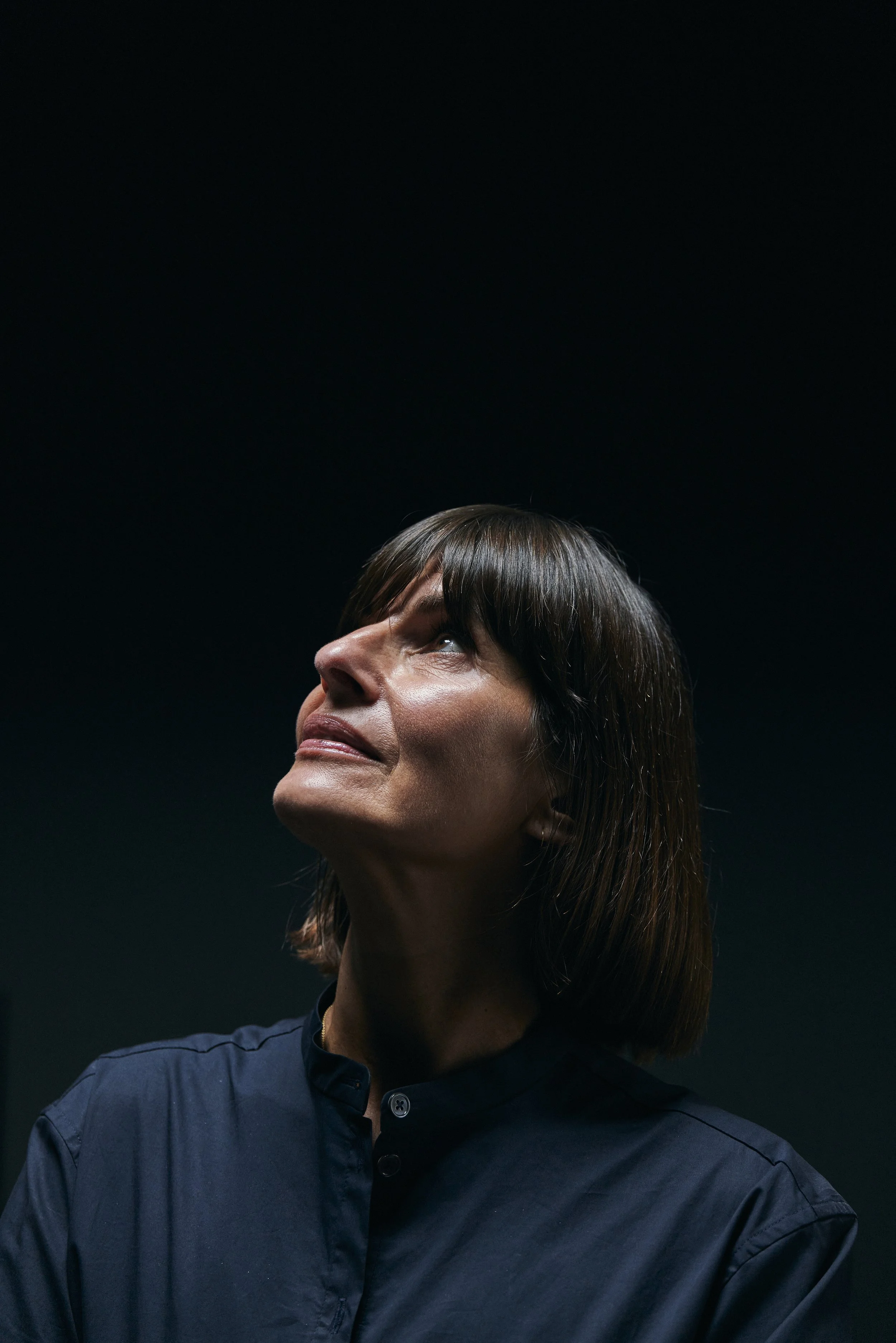 Frau mit dunklem Hintergrund schaut nach oben.