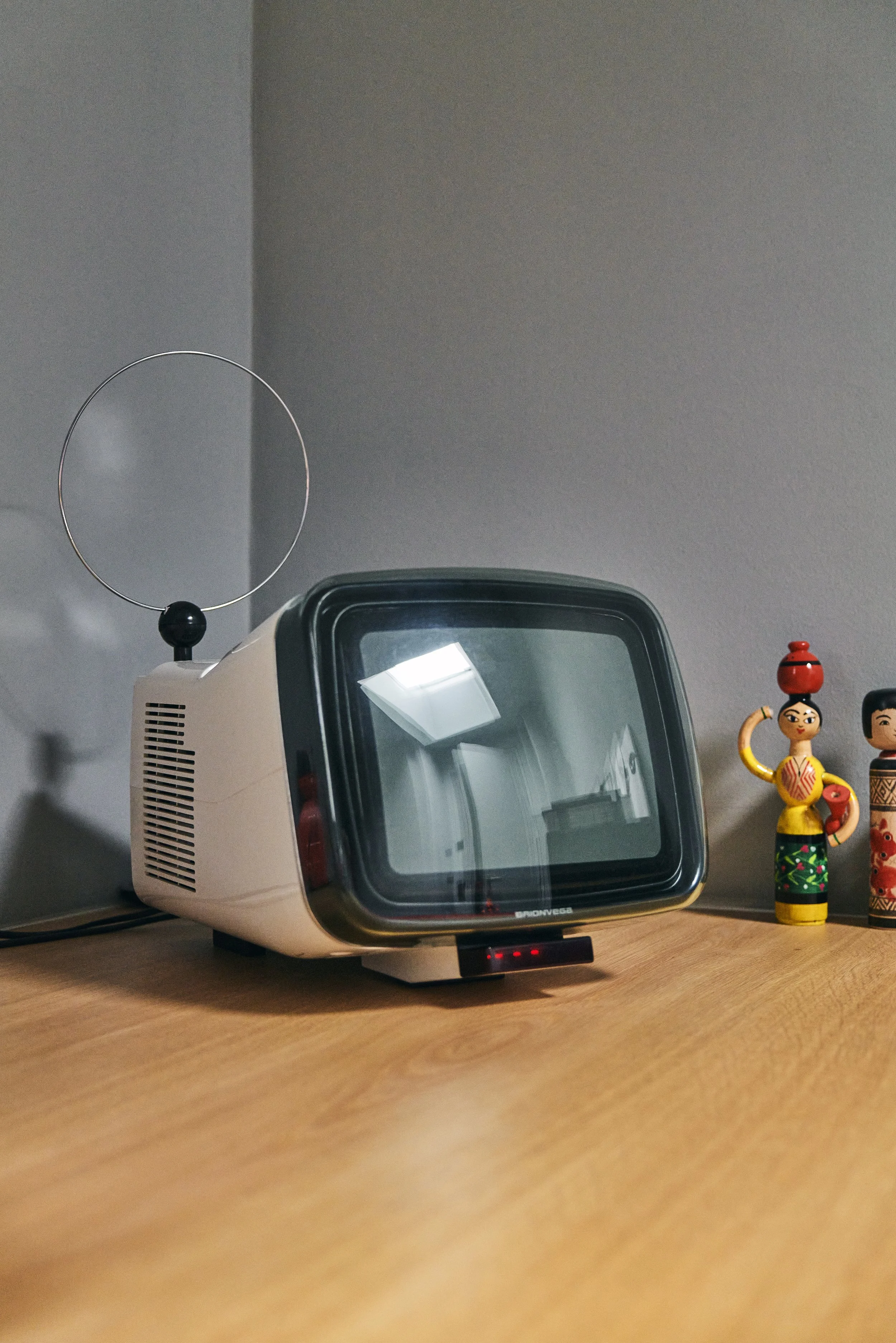 Alter Fernseher mit Antenne auf einem Tisch neben zwei bunten Holzfiguren