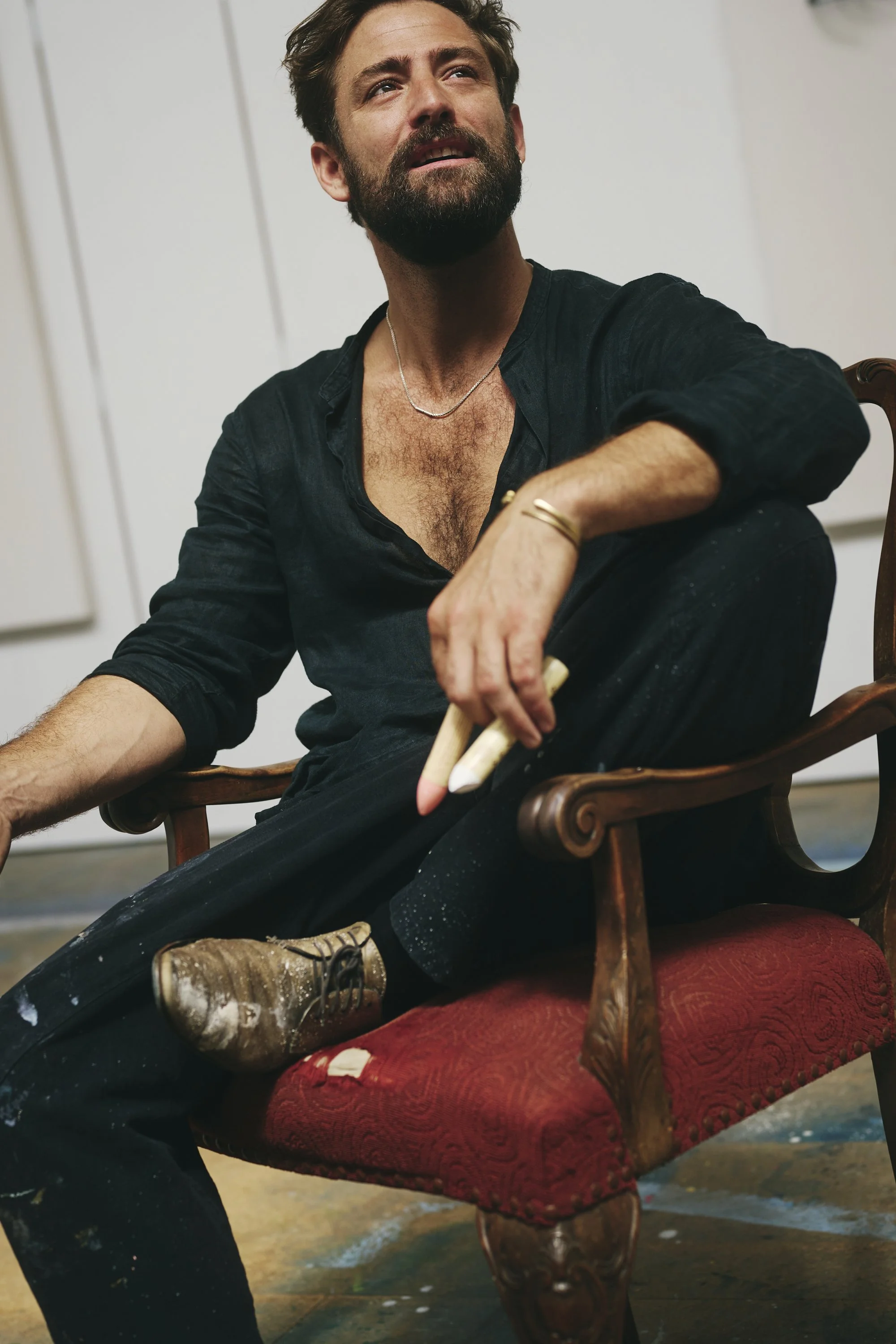 Ein Mann mit Bart sitzt in einem Sessel, trägt schwarze Kleidung und hält Kreiden in der Hand.