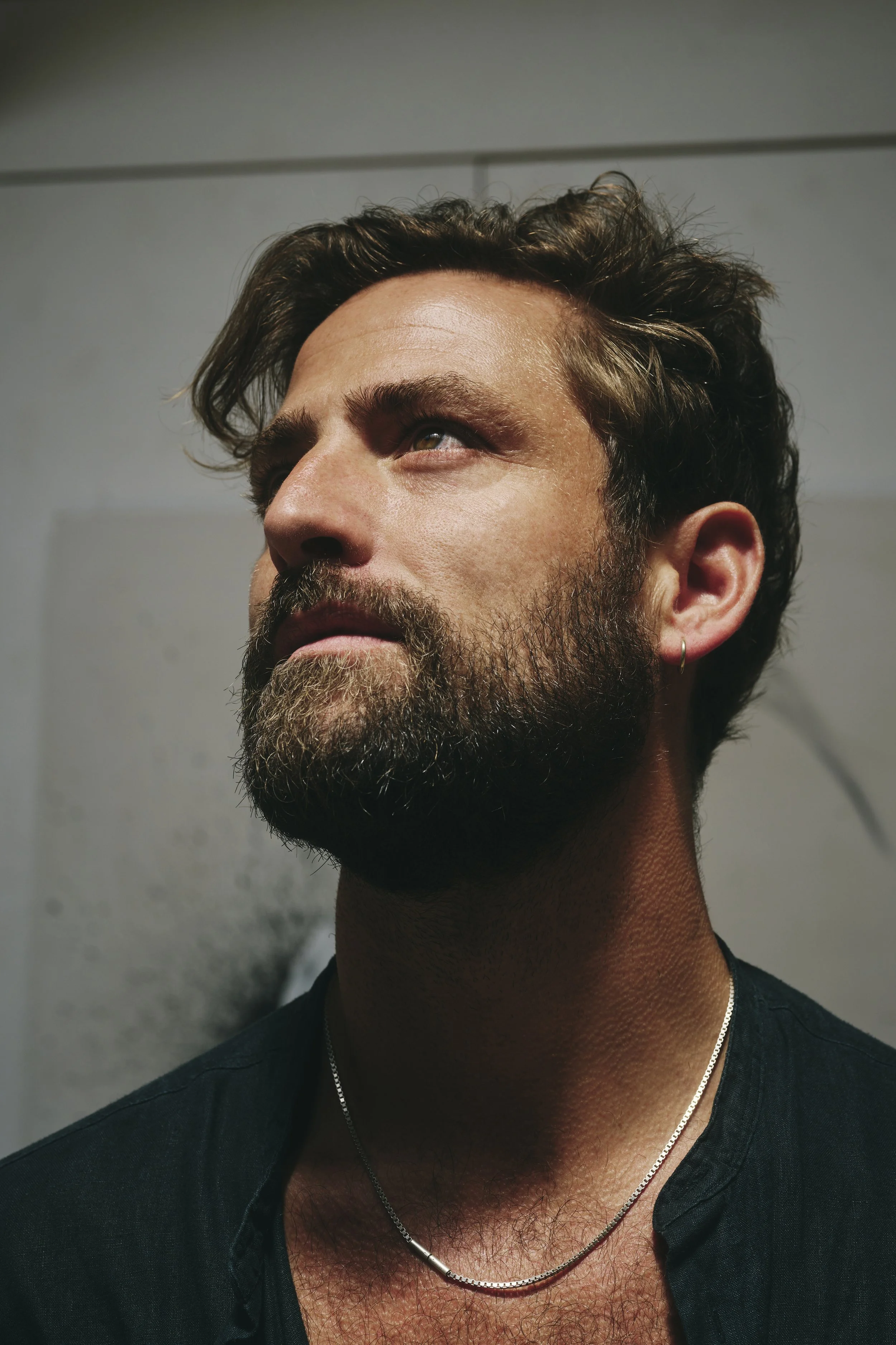 Nahaufnahme eines bärtigen Mannes mit Halskette, der nach oben schaut. Hintergrund unscharf.