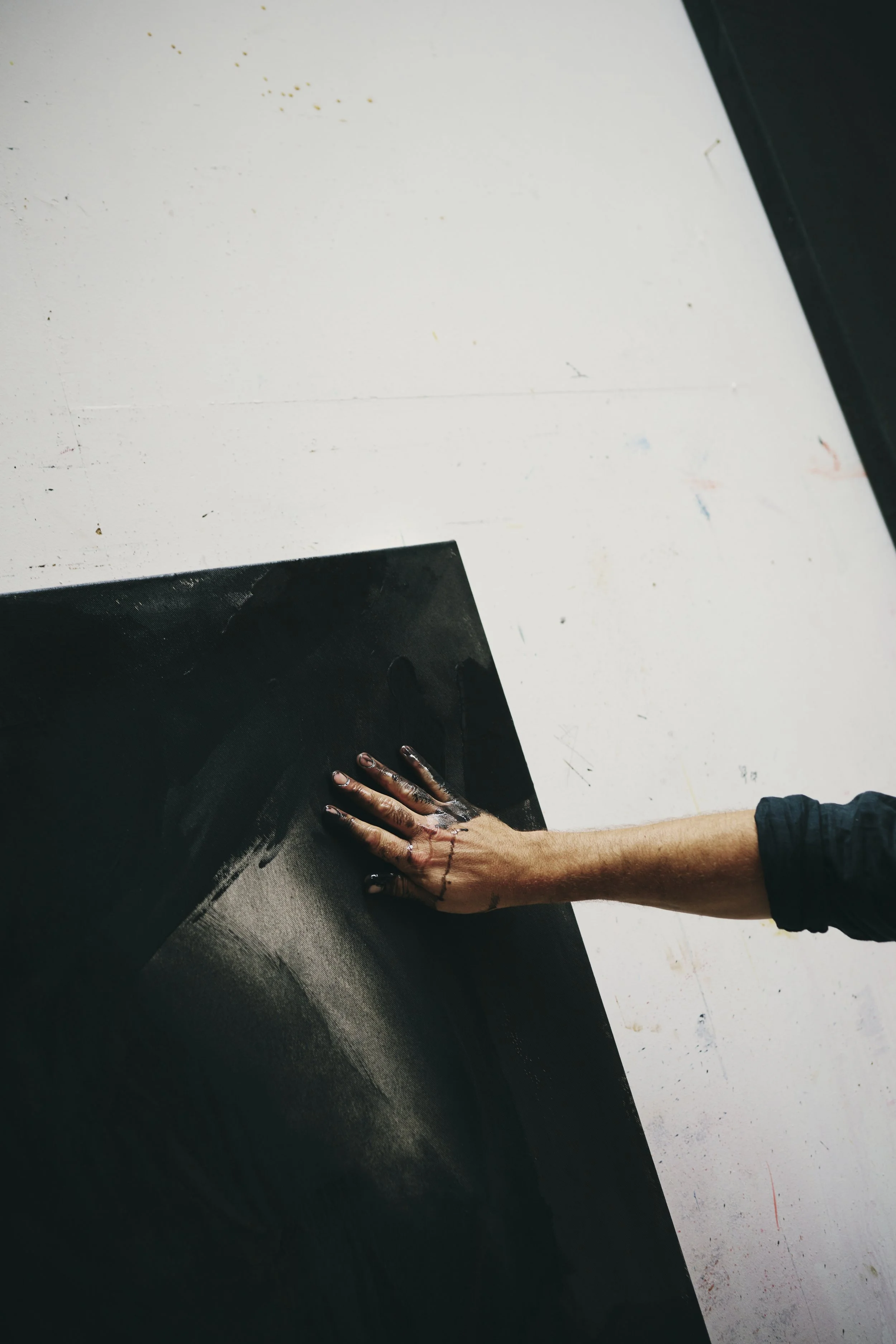 Ein Arm mit einer verschmutzten Hand berührt eine schwarze Leinwand.