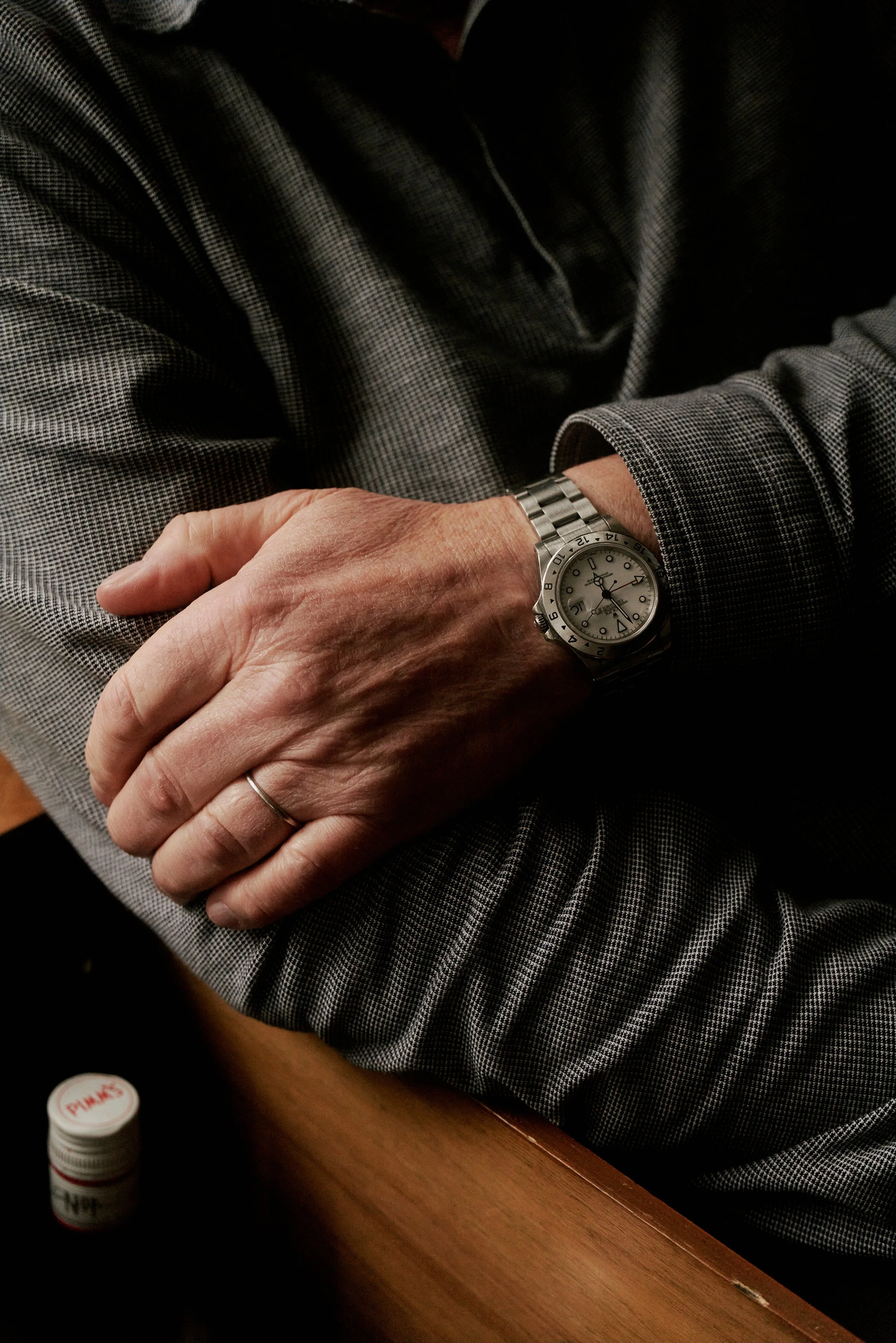 Nahaufnahme von verschränkten Armen, die eine silberne Armbanduhr und einen Ehering an der linken Hand tragen. Die Person trägt ein langärmeliges, kariertes Hemd.