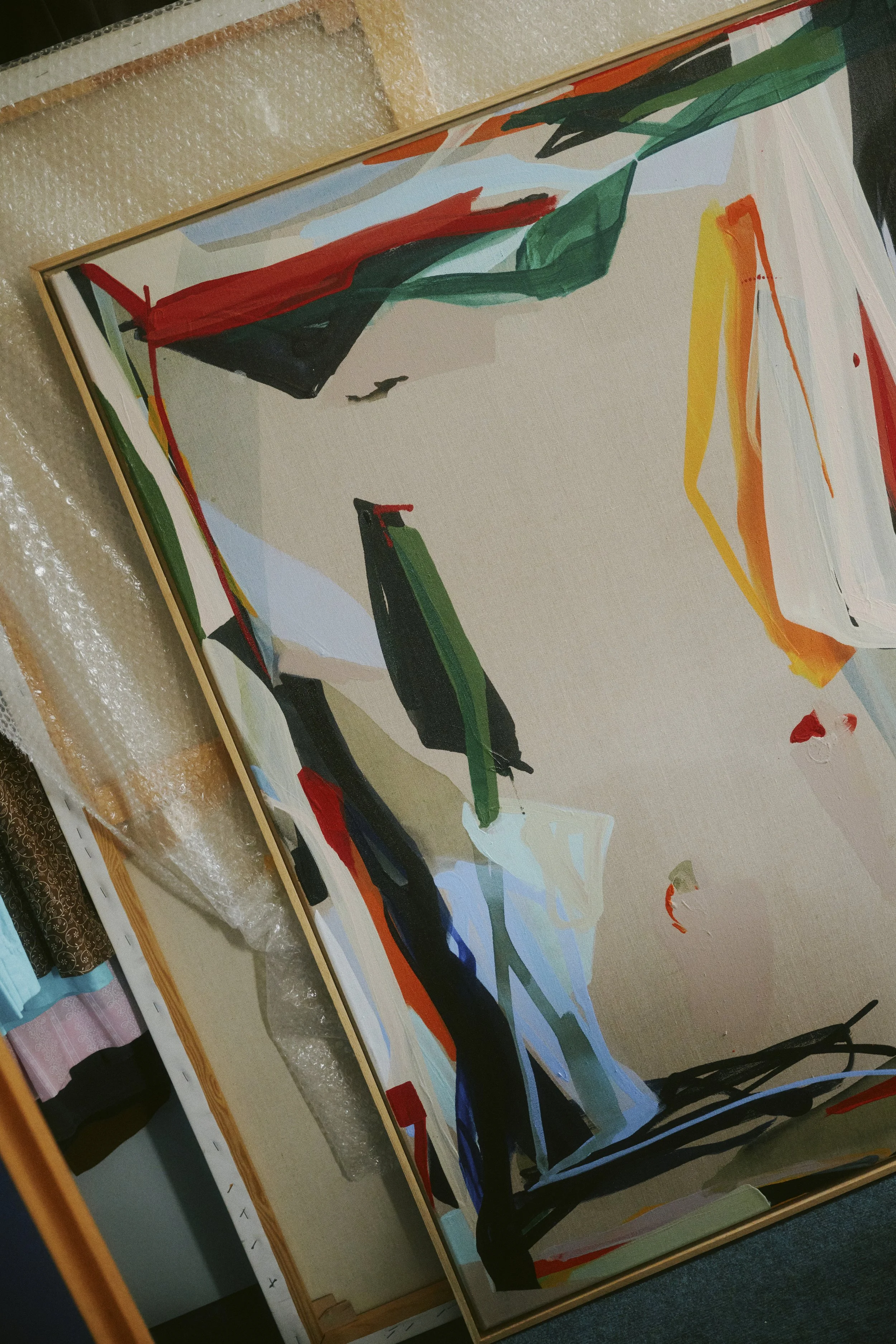 Abstraktes Gemälde mit kräftigen, bunten Pinselstrichen, das gegen ein weiteres Bild und Luftpolsterfolie lehnt.