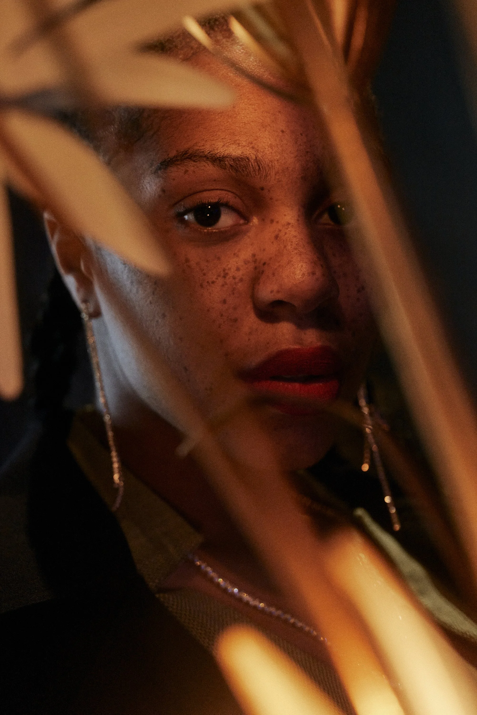 Porträt QUEEN Lizzy mit geflochtenem Haar, die durch beleuchtete Pflanzenstängel schaut.