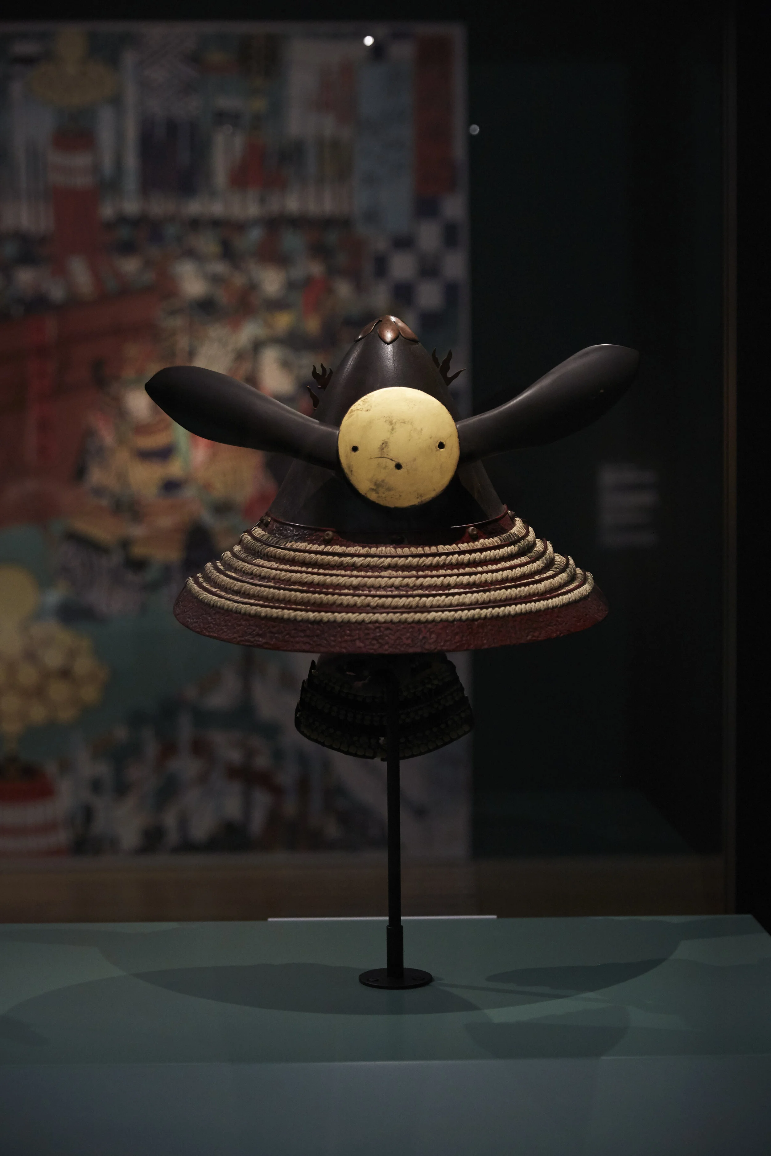 Samurai-Helm mit markanten Hörnern und gelber Plakette, ausgestellt in einem Museum vor einem unscharfen Hintergrund.