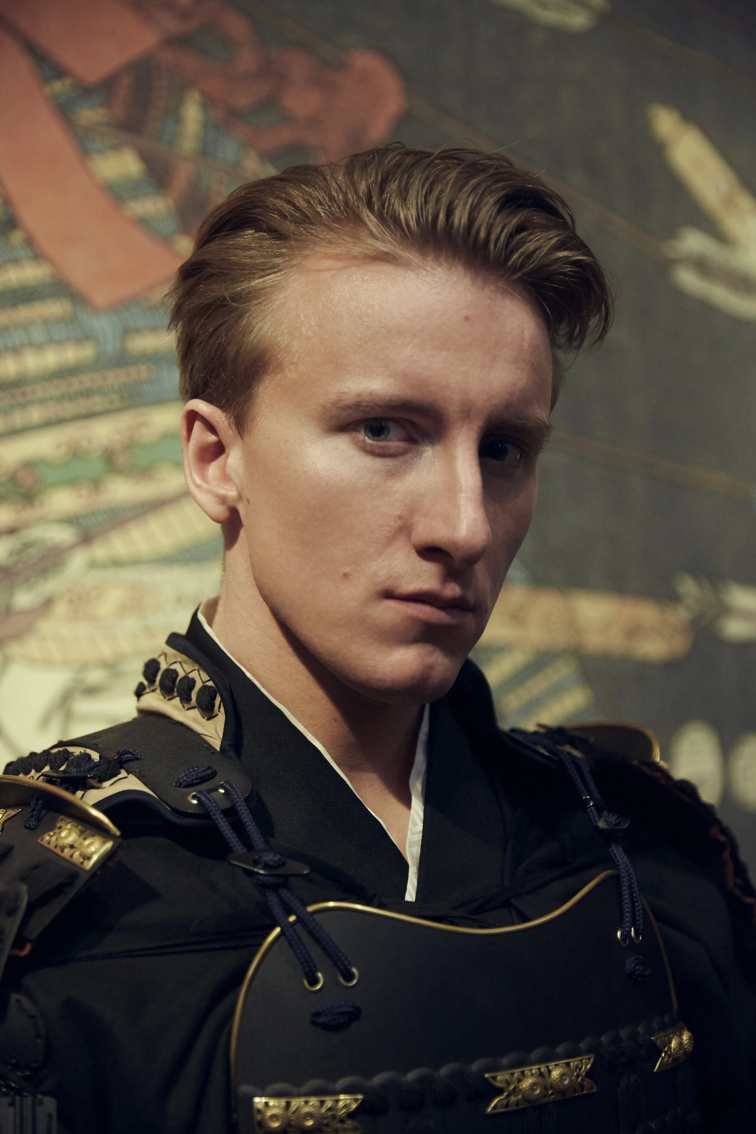 Porträt eines Mannes in traditioneller Samurai-Rüstung vor einem kunstvollen Hintergrund.