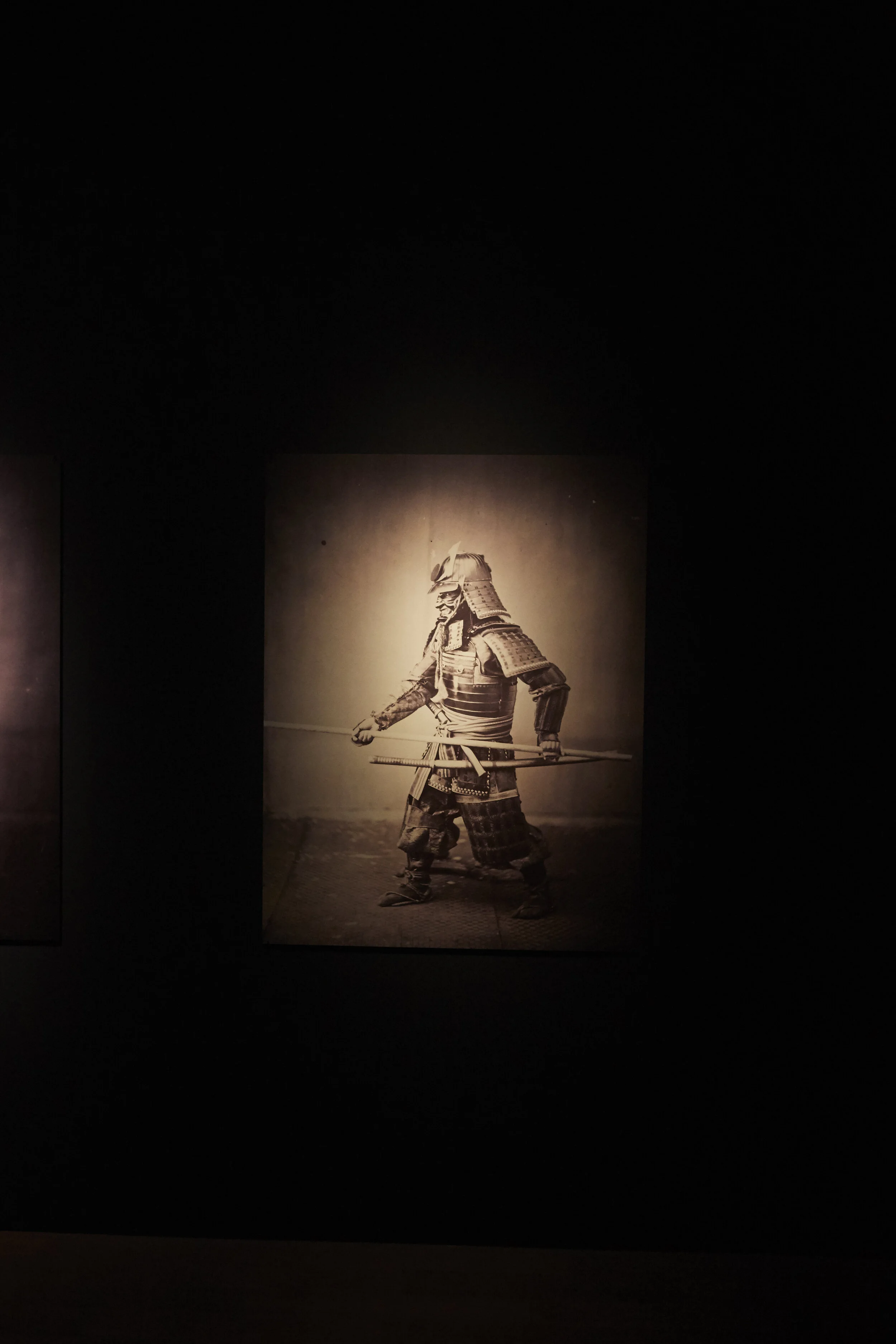 Ein Bild zeigt einen traditionellen Samurai in Rüstung mit Schwert, ausgestellt in einem dunklen Raum.