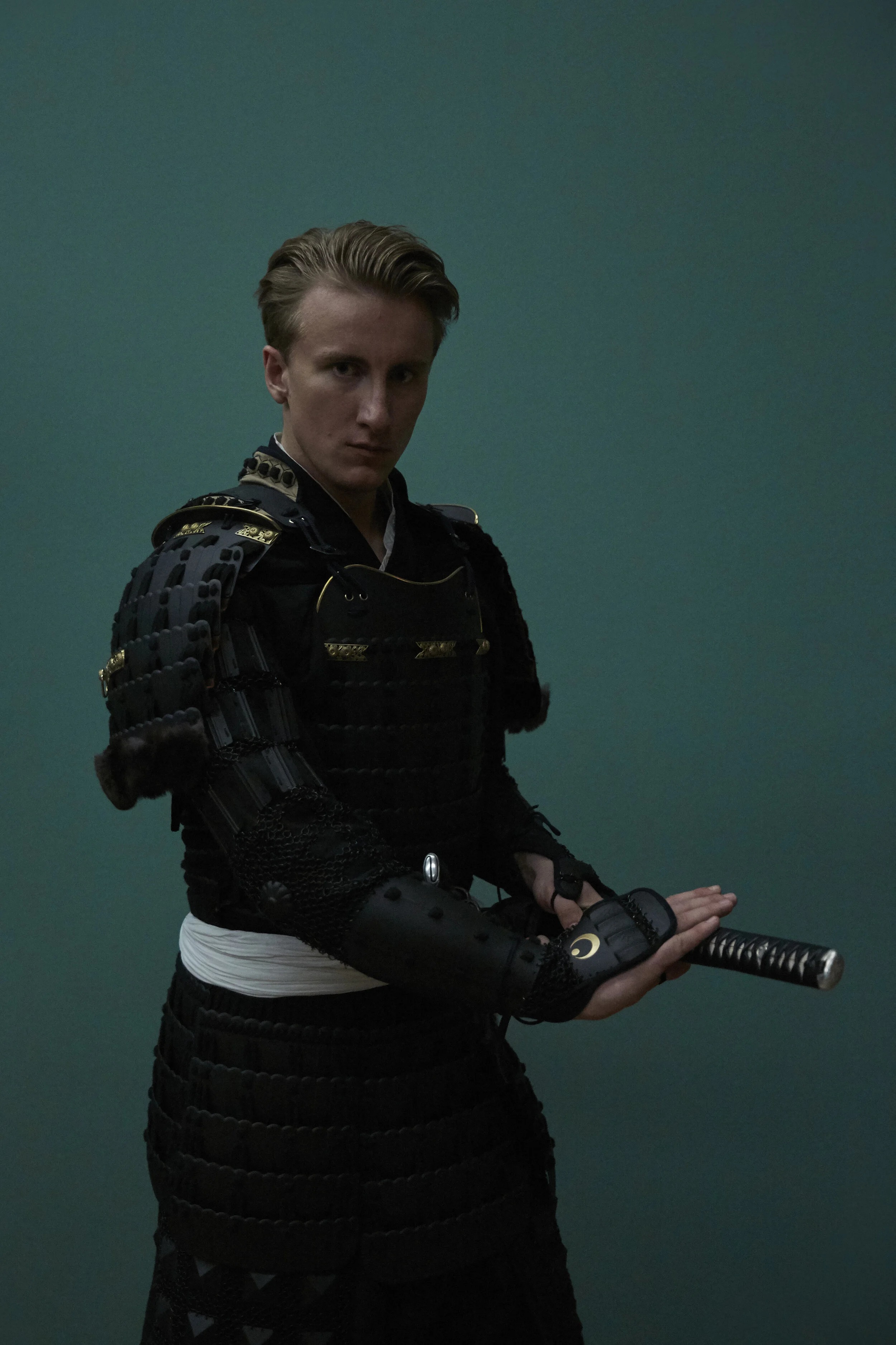 Person in traditioneller Samurai-Rüstung mit Schwert, vor grauem Hintergrund.