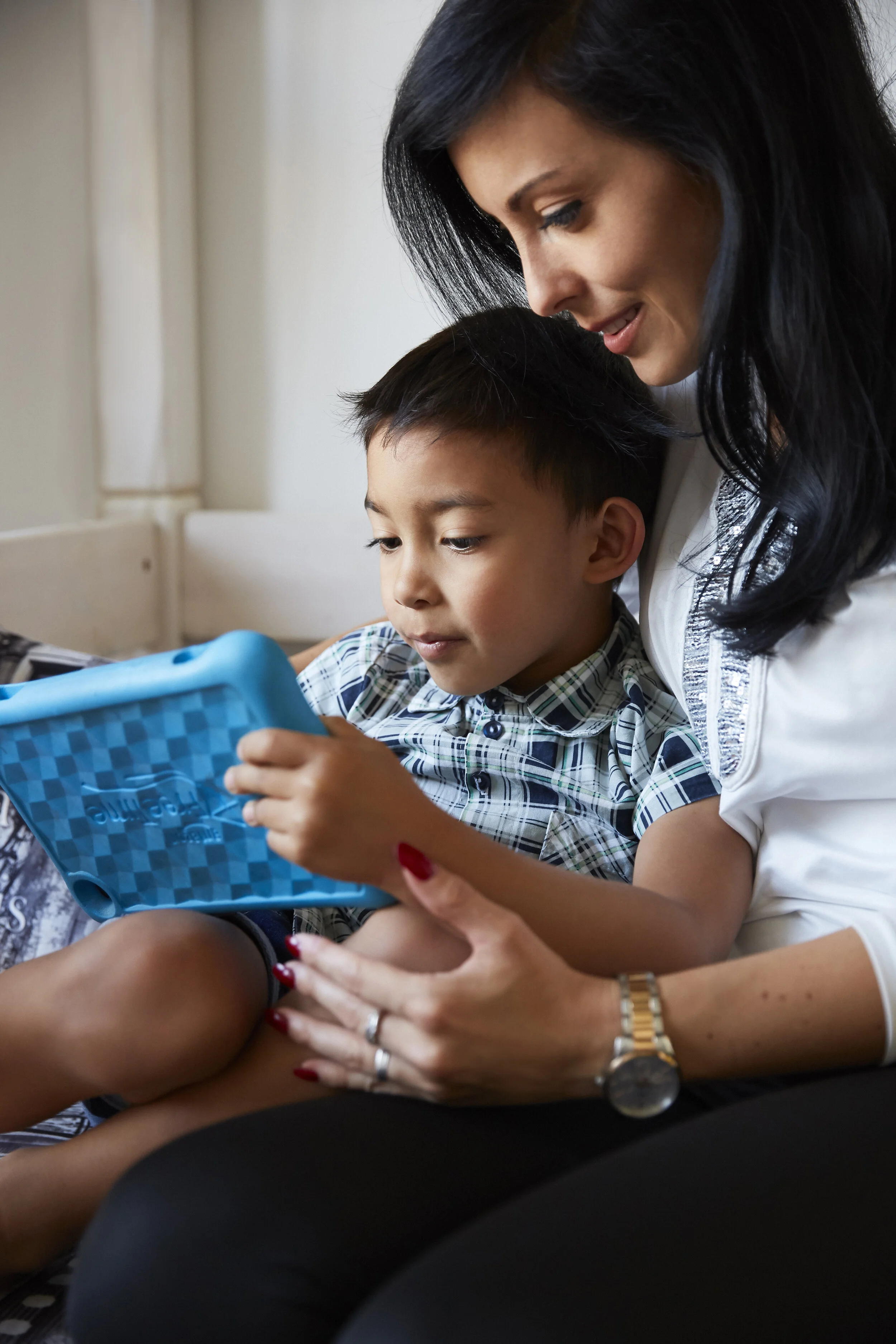 Eine Frau und ein Kind sitzen zusammen und schauen auf ein Tablet in einer blauen Hülle.