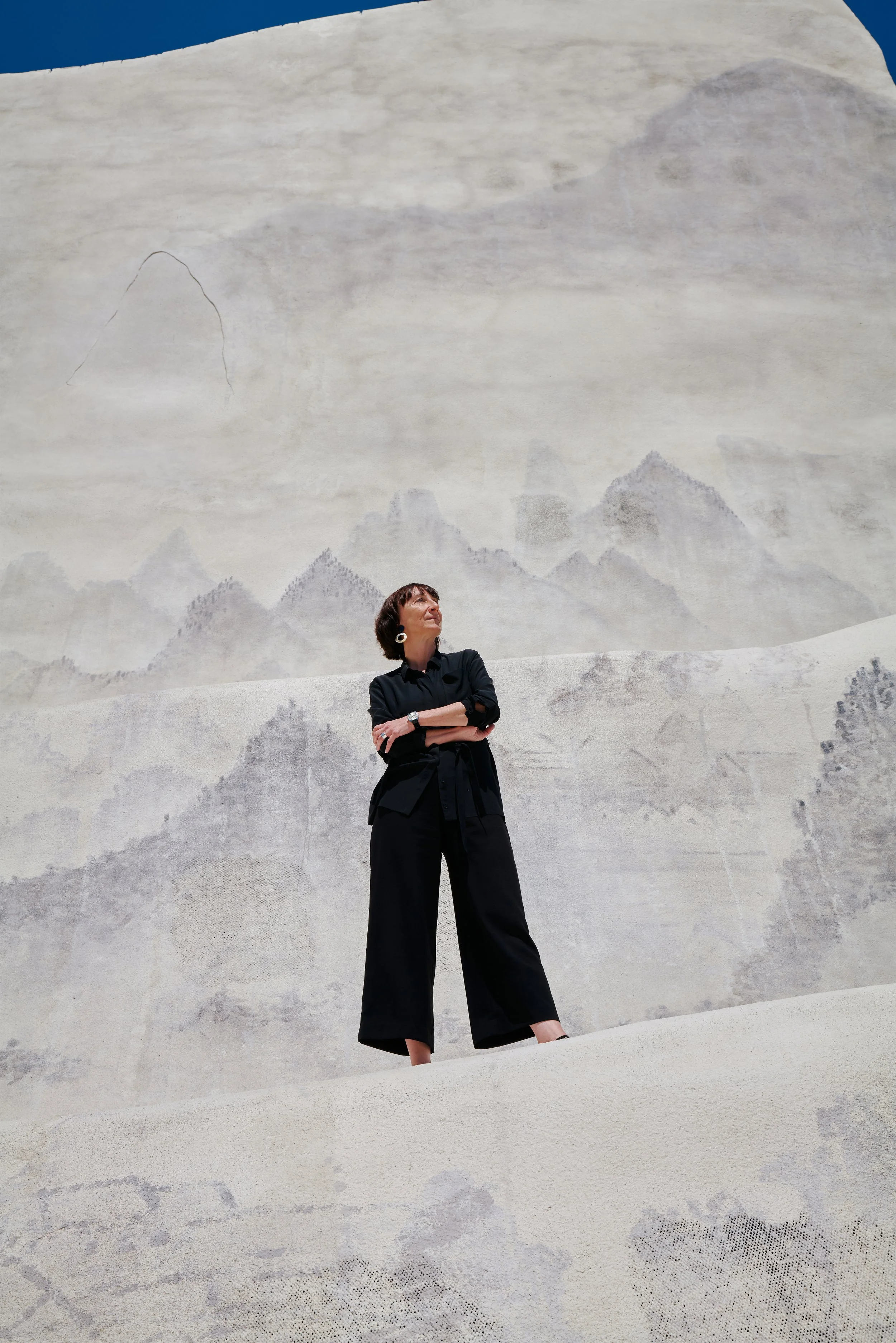Elisabeth Sobotka in schwarzer Kleidung steht vor einer großflächigen, strukturierten weißen Wand. Der Himmel ist im Hintergrund blau.